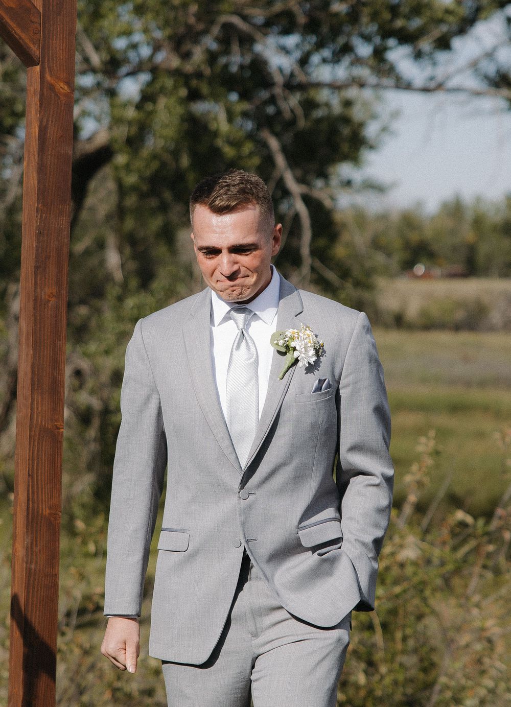 Emotional groom in light gray suit with boutonniere trying to hold back tears at outdoor wedding ceremony.
Great Falls Montana, Milo Creek W