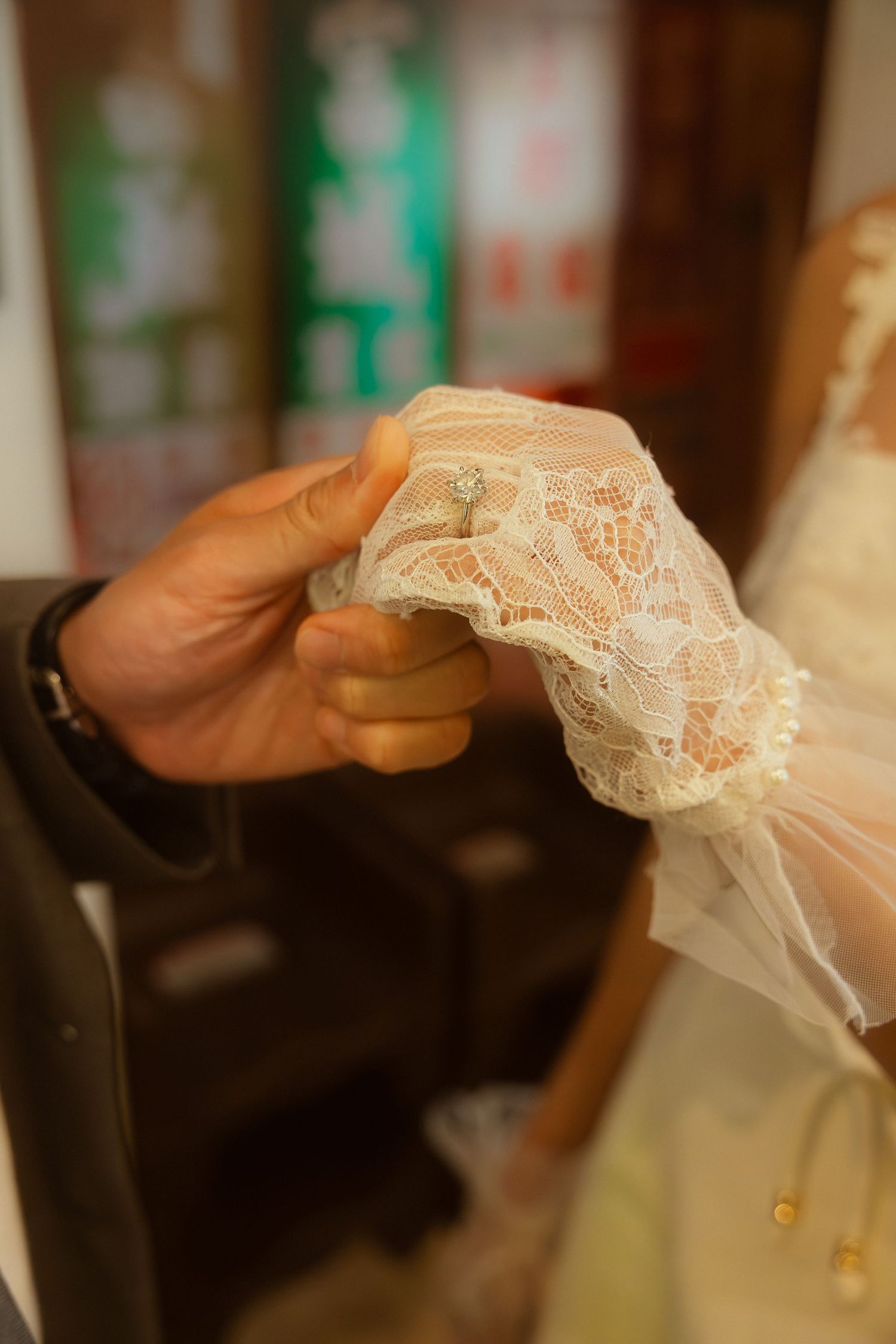 Close-up of a groom holding a bride's lace-gloved hand during a wedding ceremony.