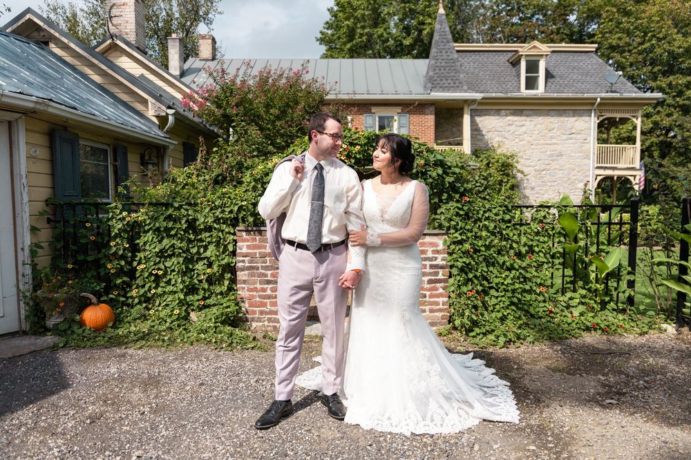 Bride and groom laughing together outdoors in front of a charming stone house with lush greenery on their wedding day.