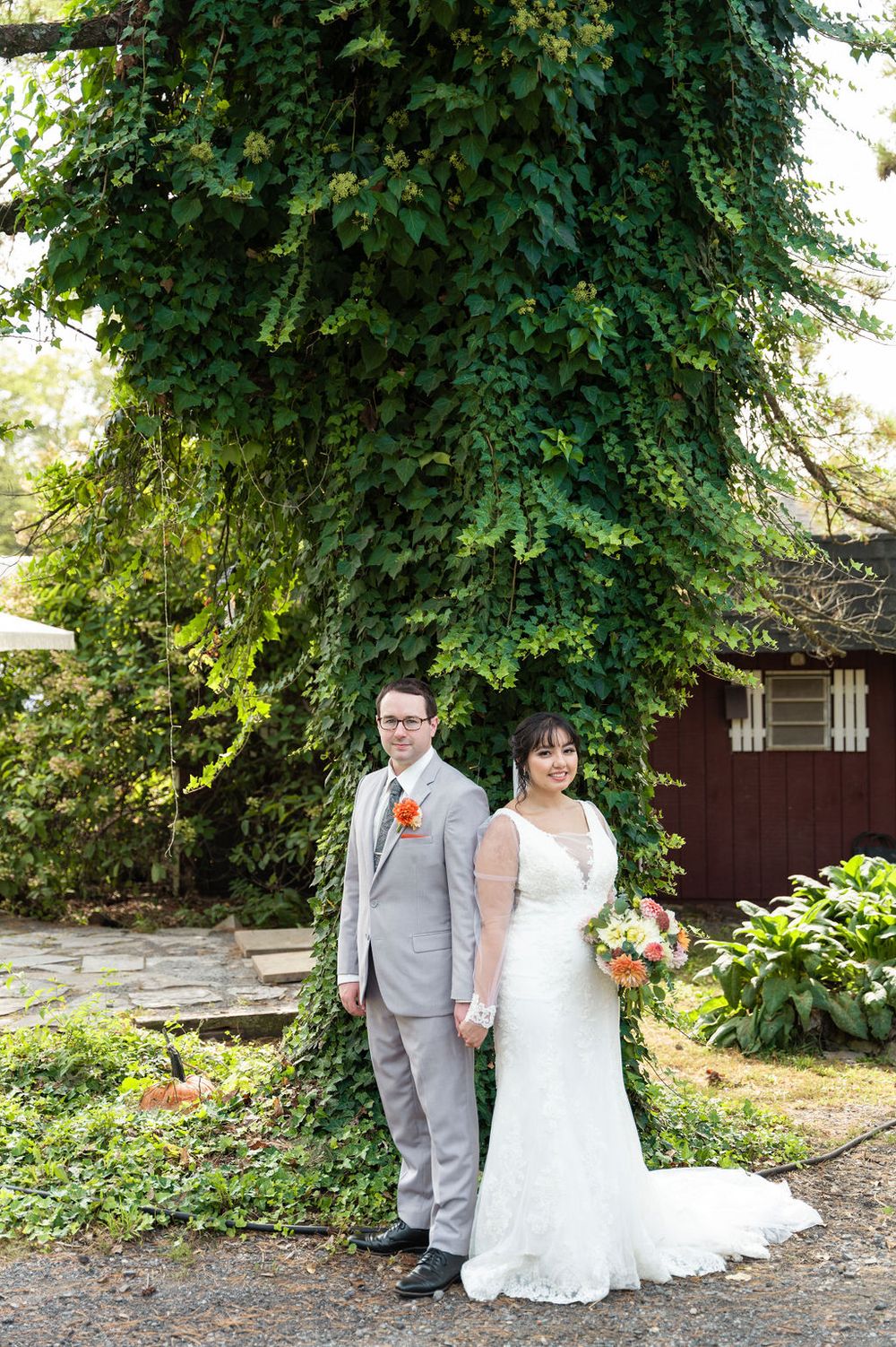 Bride and groom pose together in front of ivy-covered tree at outdoor wedding venue.
