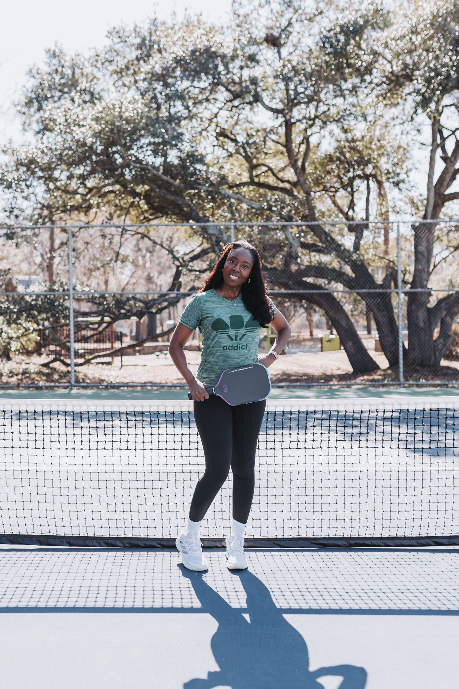 Woman in green graphic tee holding a pickleball paddle on an outdoor court near a net.