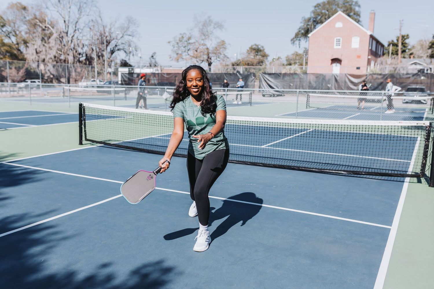 Woman playing pickleball on blue outdoor court, holding paddle ready to hit in sunny weather.