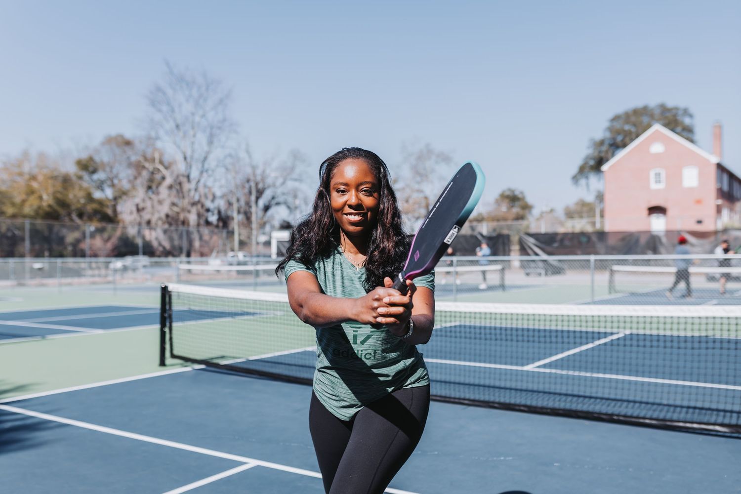 Young Black woman smiling while playing pickleball on an outdoor court on a sunny day.