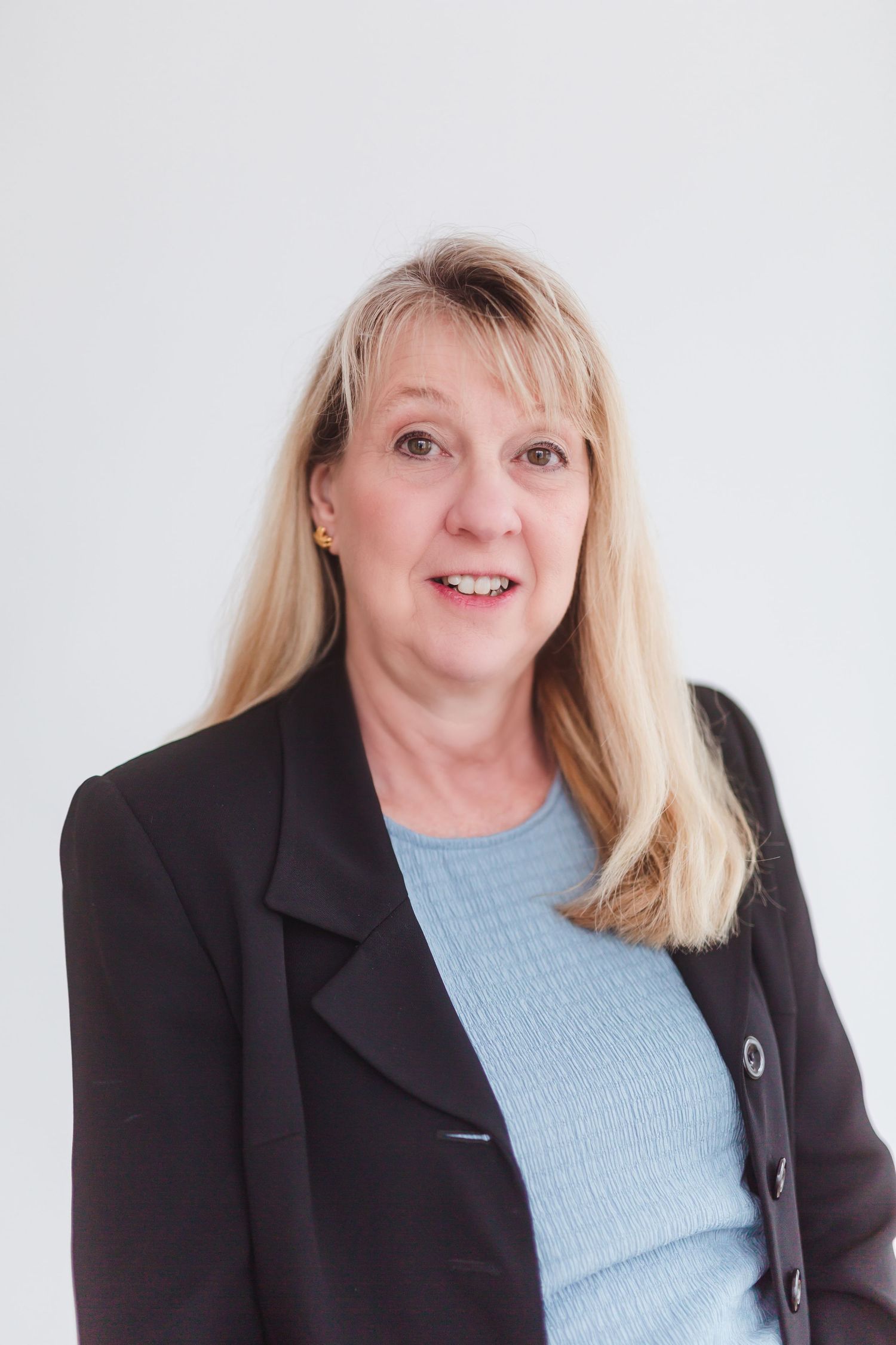 Professional headshot of a smiling middle-aged blonde woman in a black blazer and light blue top against a white background.