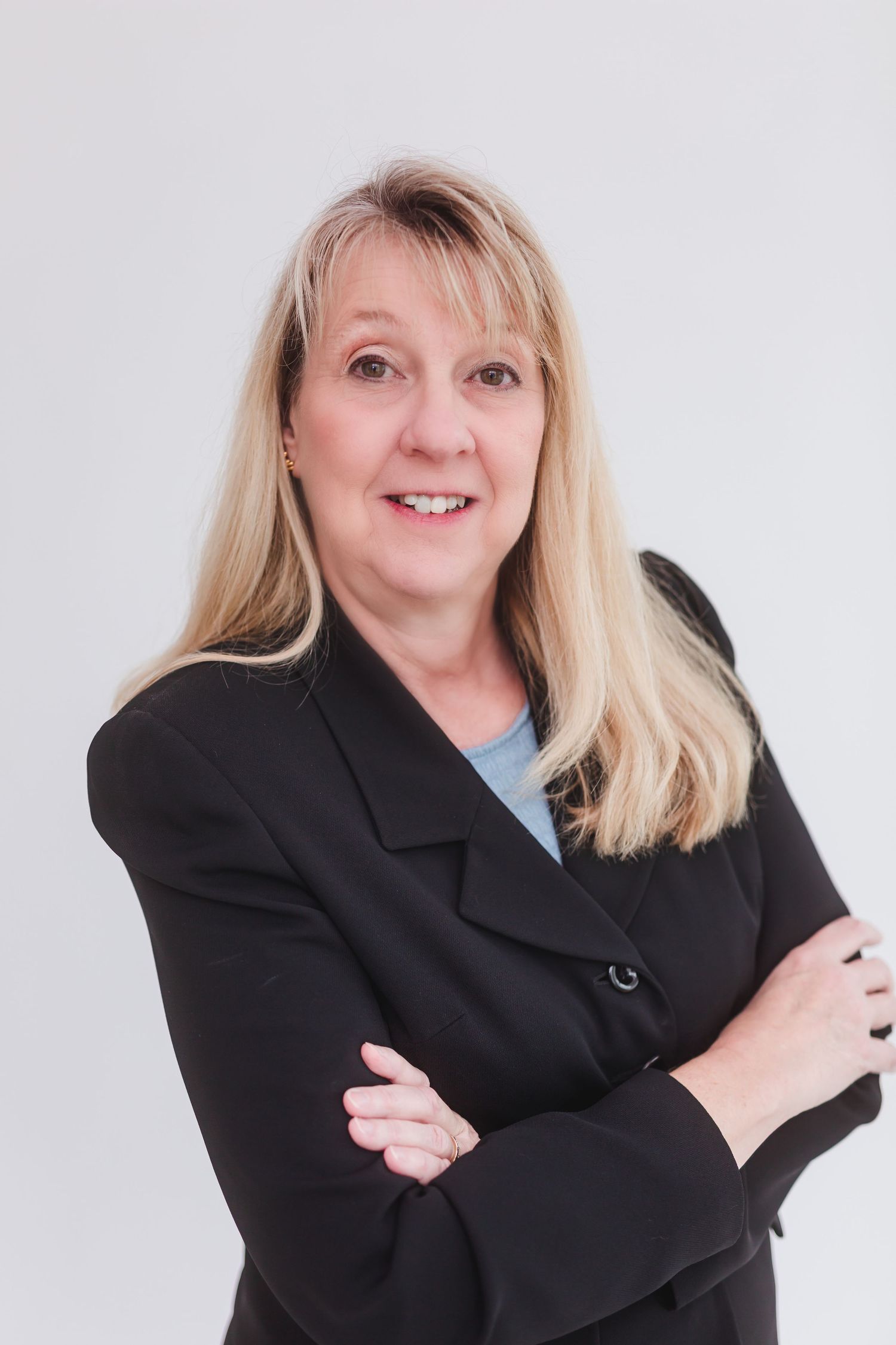 Professional businesswoman with blonde hair in black blazer smiling with arms crossed against white background.