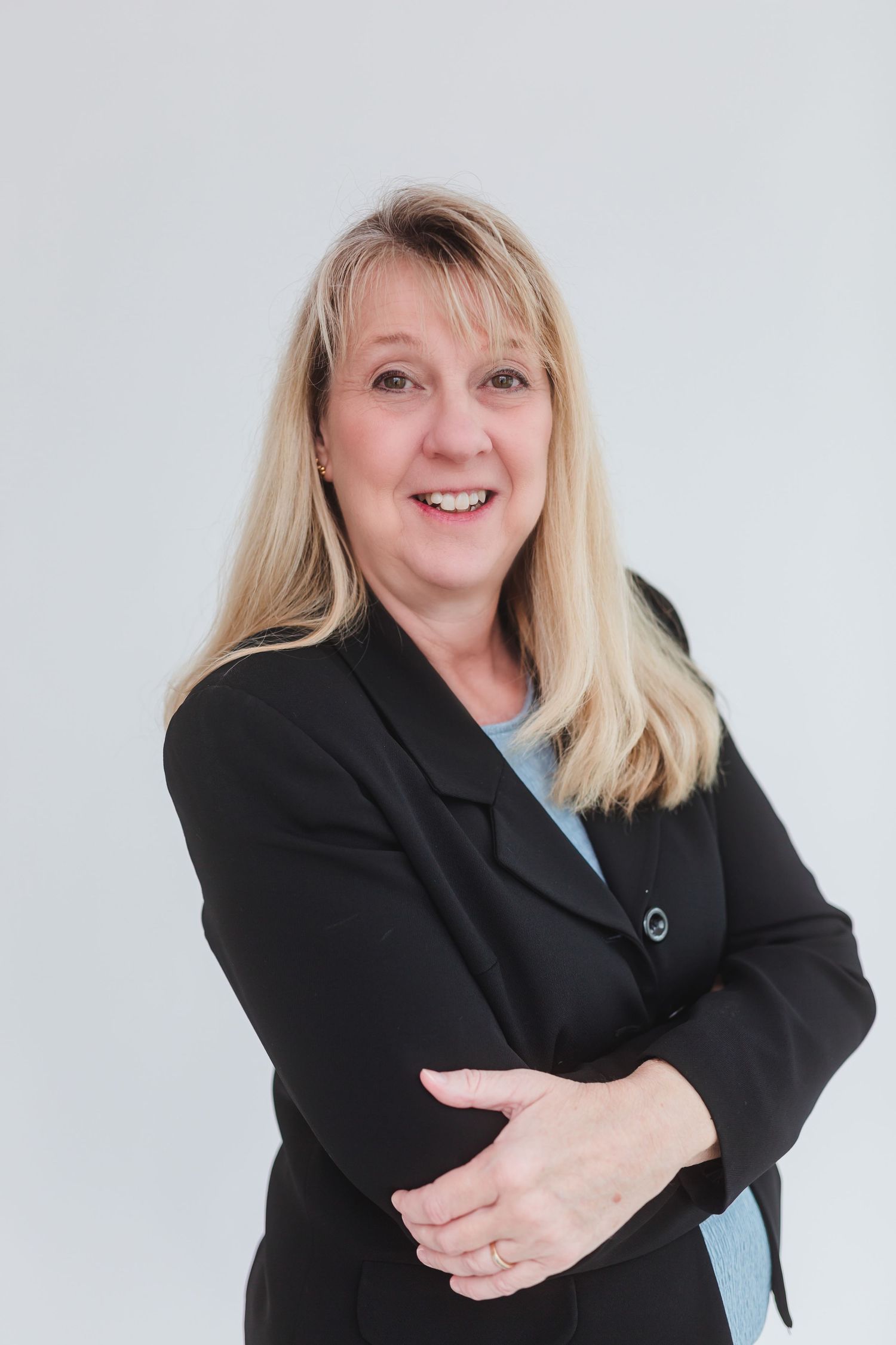 Professional woman in black blazer smiling with arms crossed against white background.