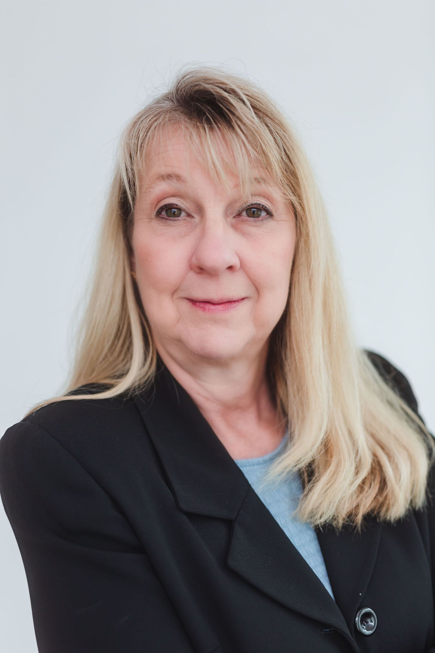 Professional headshot of a blonde woman in a black blazer smiling against a light gray background.