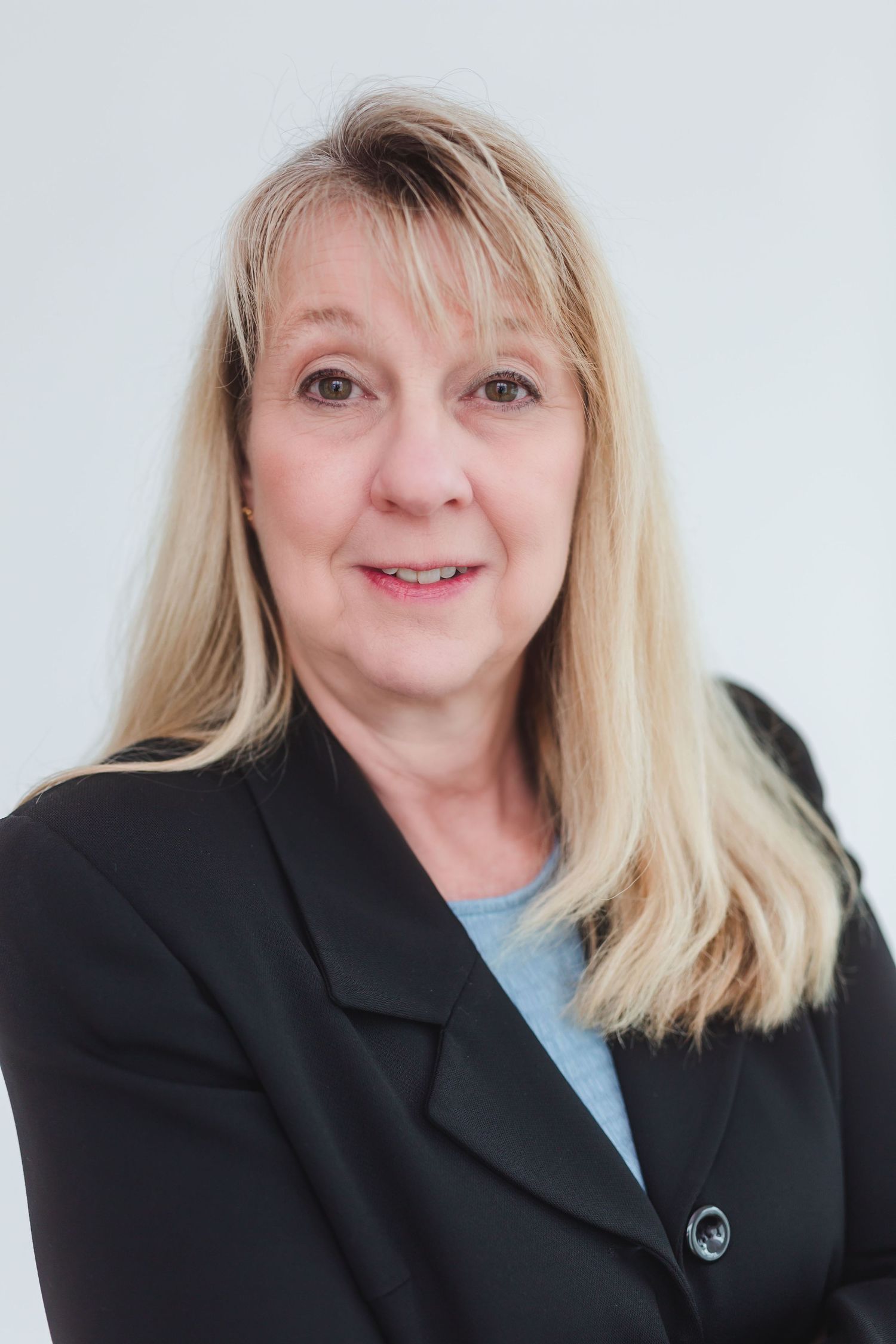 Professional headshot of a smiling blonde woman in a black blazer against a light gray background.