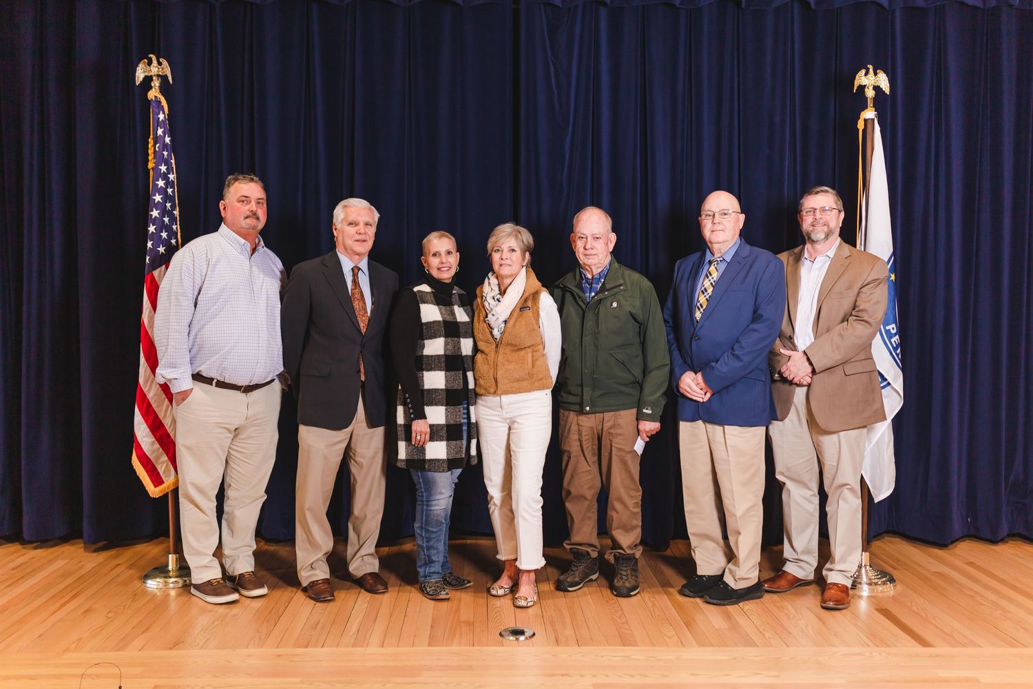 Seven officials standing together on stage flanked by American and organizational flags.