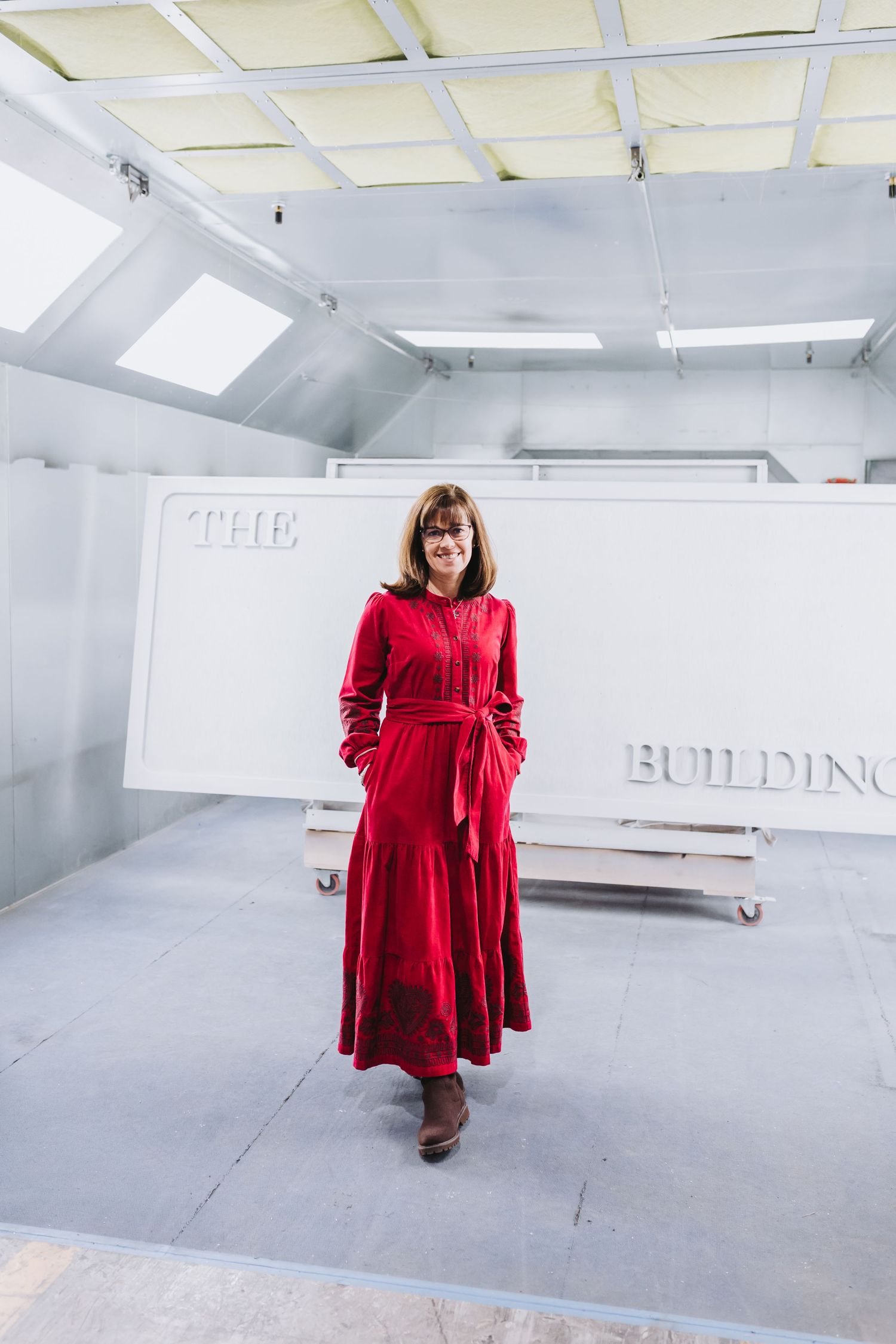 Woman in red maxi dress standing confidently in a white industrial space with 'The Building' signage.