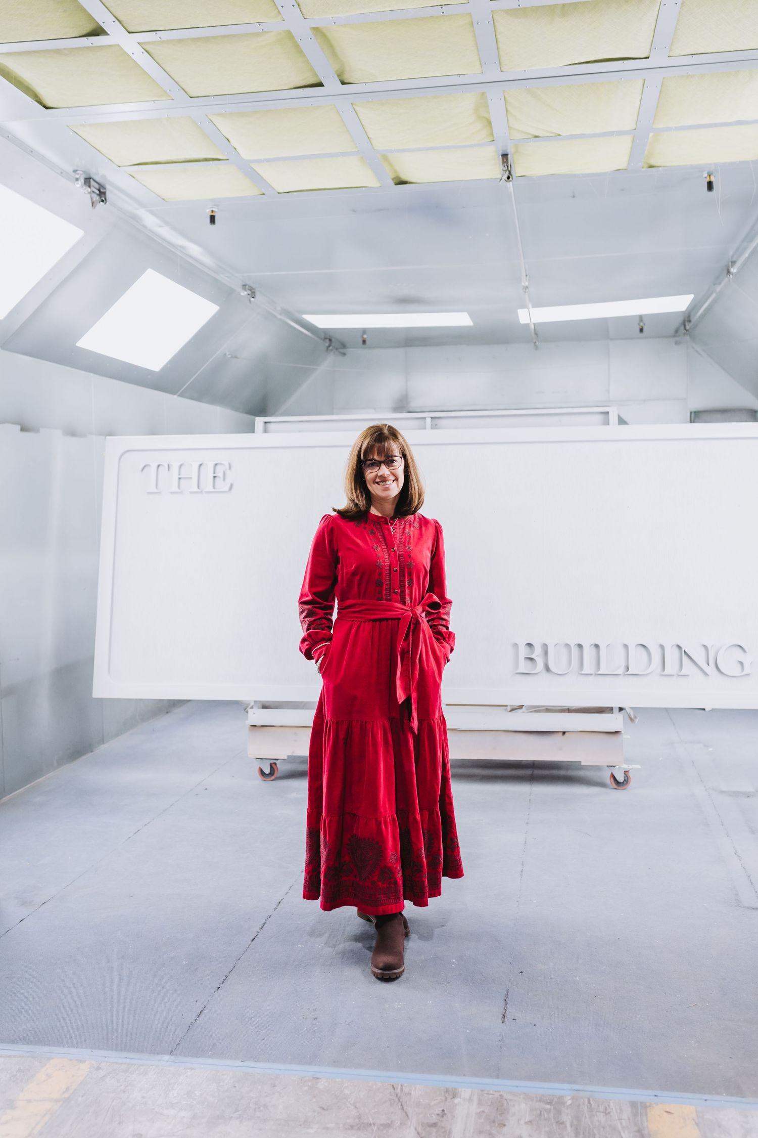 Woman in red dress standing in front of a white sign reading The Building in a bright studio space.
