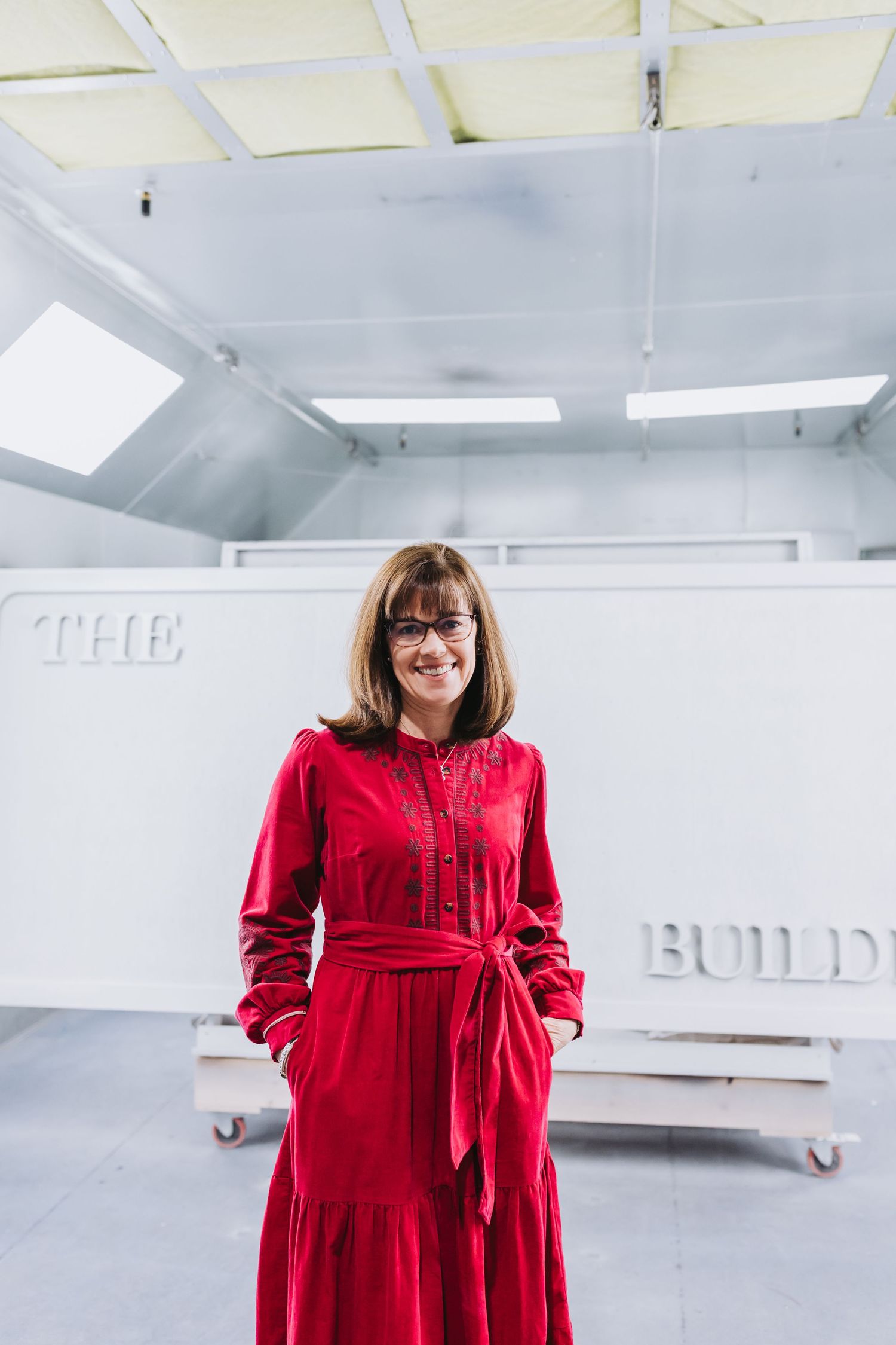 Woman in red dress smiling in front of The Building sign in a white studio space.