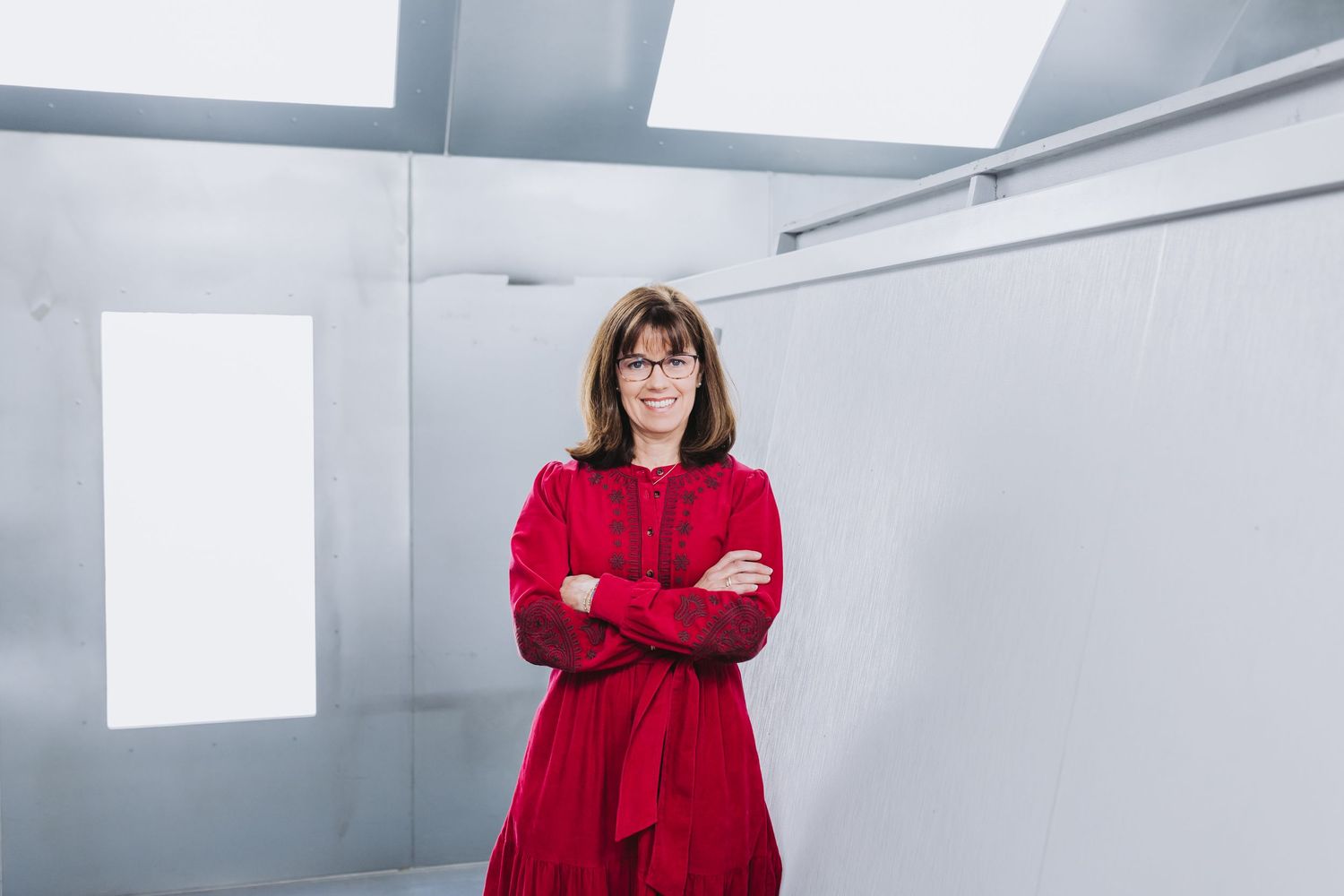 Woman in red dress with arms crossed standing confidently in a modern white gallery space.