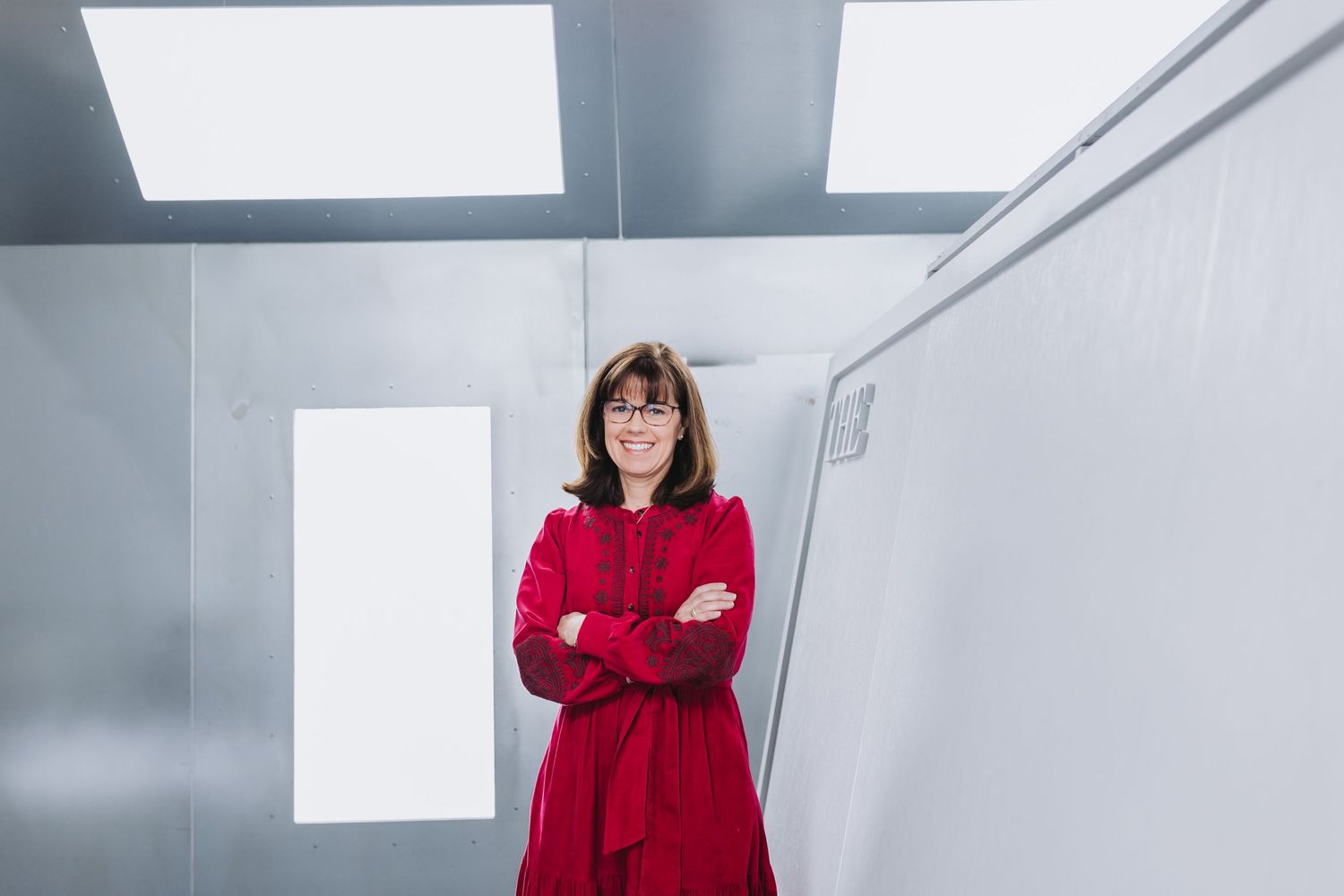 Woman in red dress with arms crossed smiling in a modern white room with bright lighting.