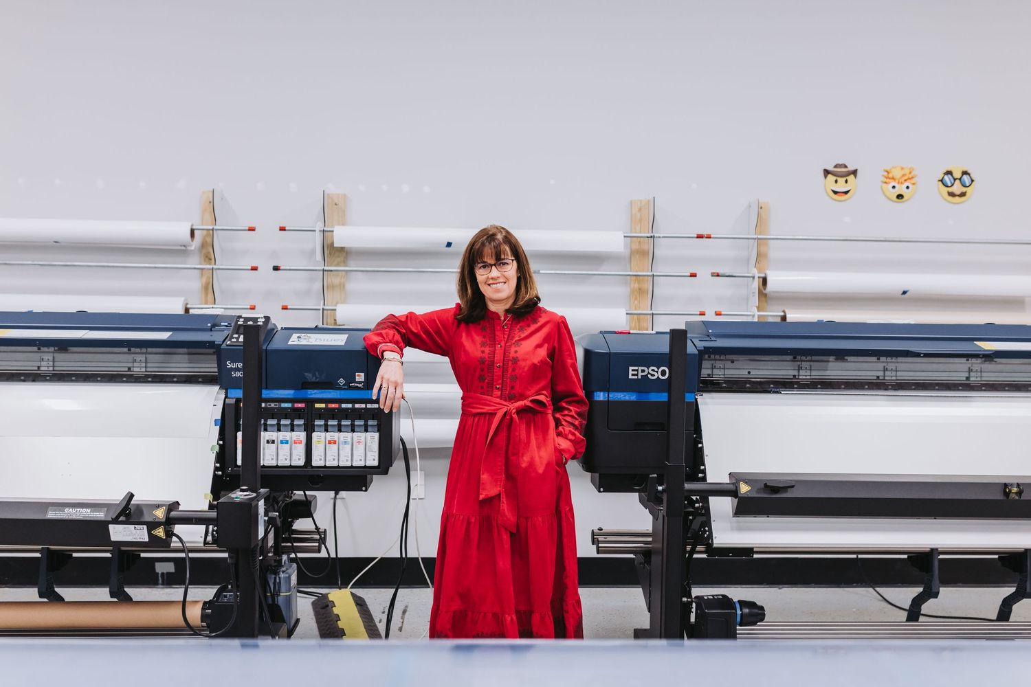 Woman in red dress standing between two Epson large format printers in a bright studio.