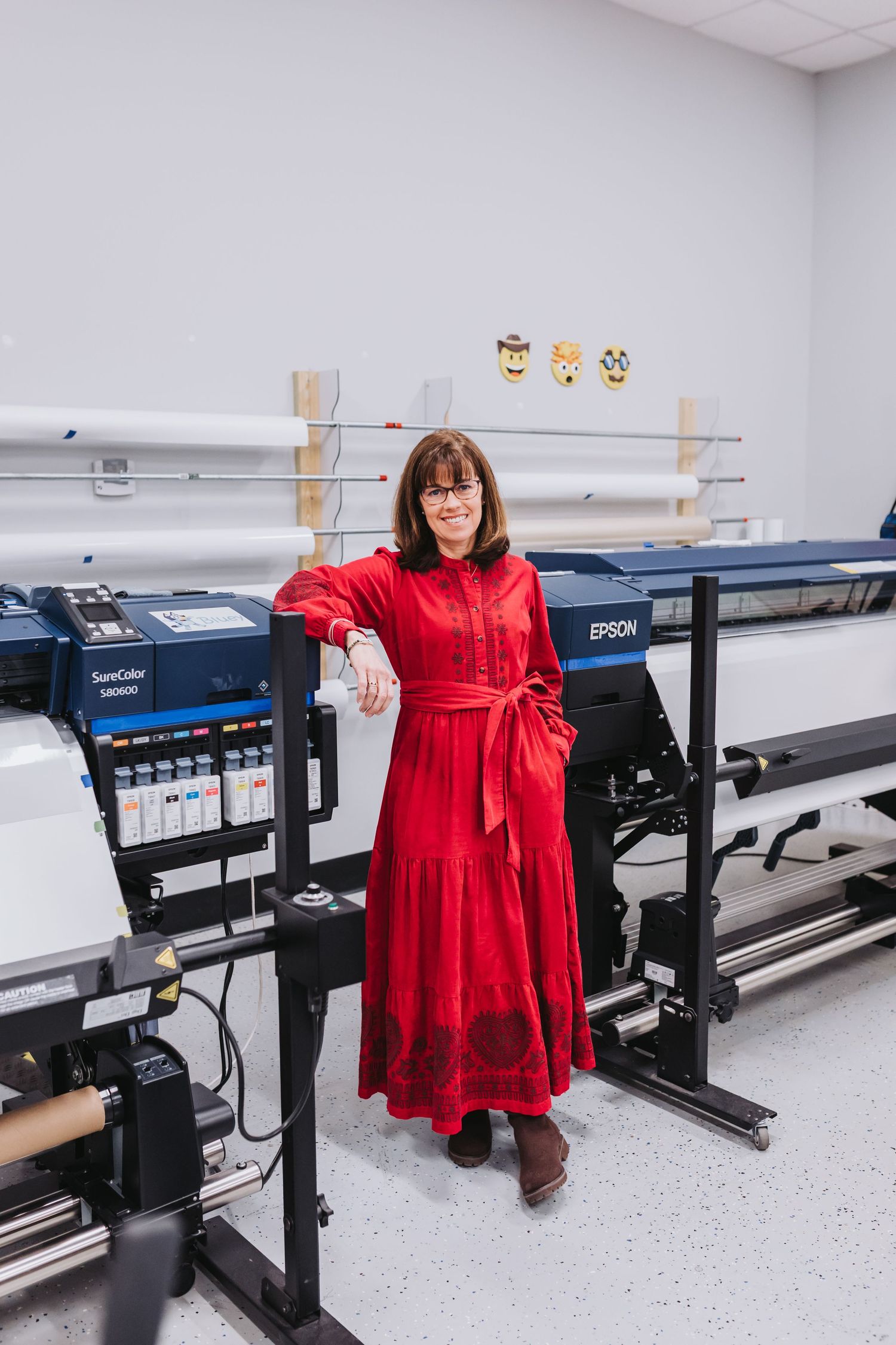 Woman in red dress posing beside Epson SureColor large format printer in a professional print studio.