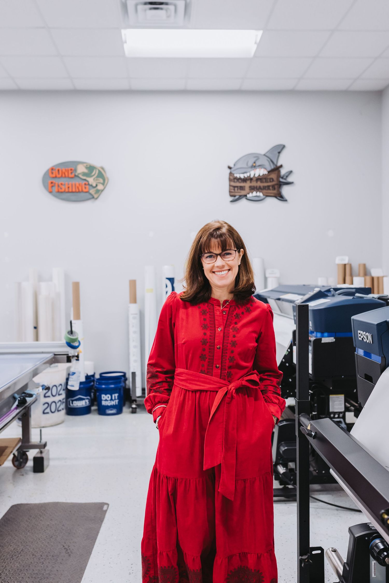 Woman in red dress smiling in a print shop with Epson printer and decorative signs on the wall.
