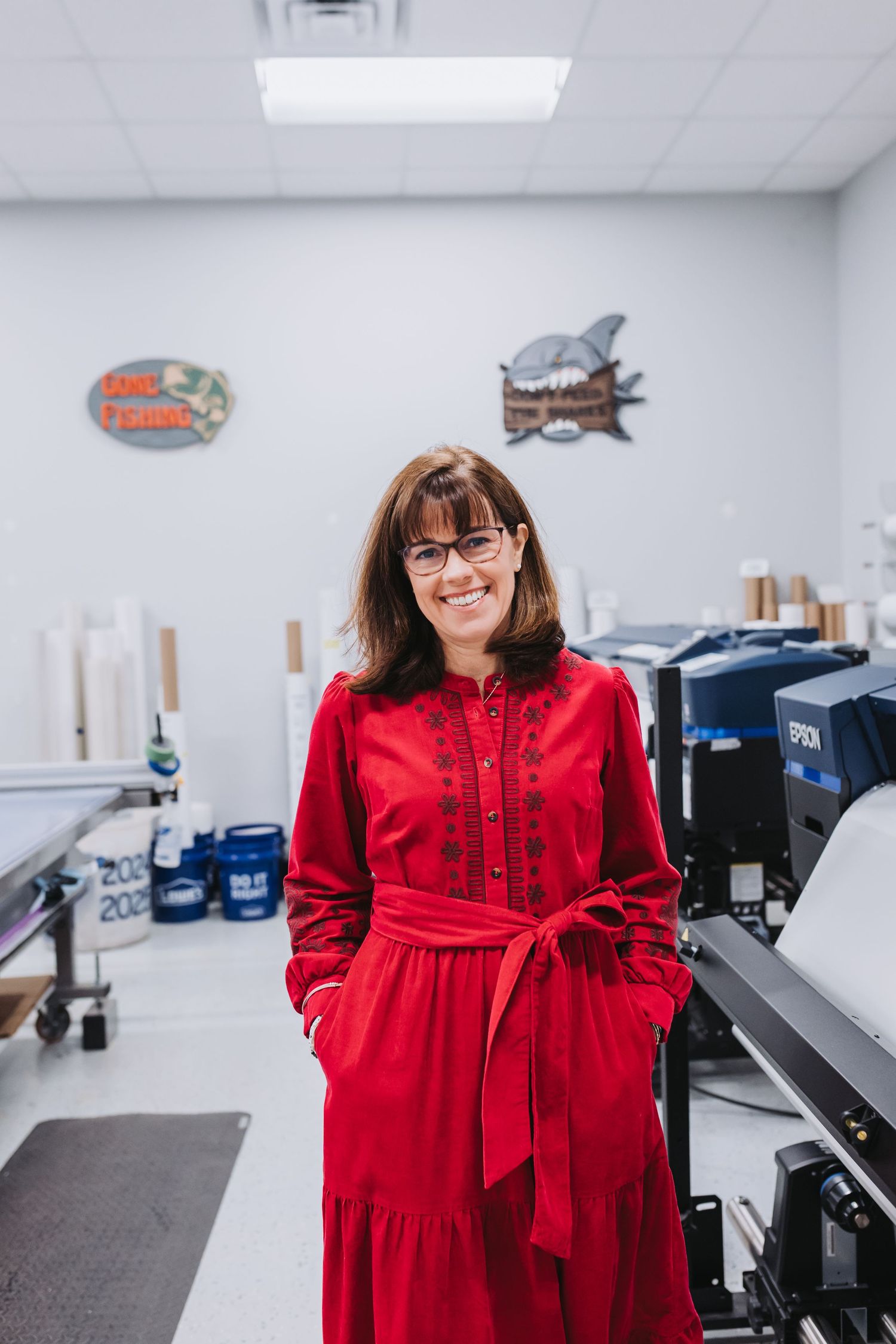 Woman in red dress smiling in a print shop with an Epson printer and decorative signs on the wall.