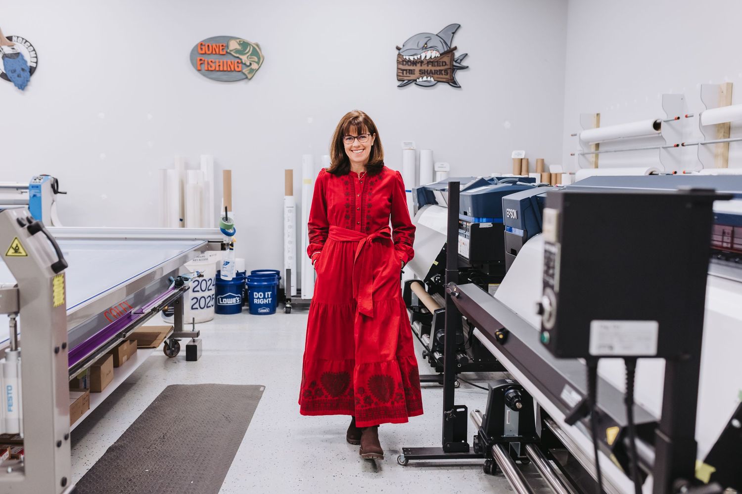 Woman in red dress walks through a professional printing facility with large format printers and supplies.