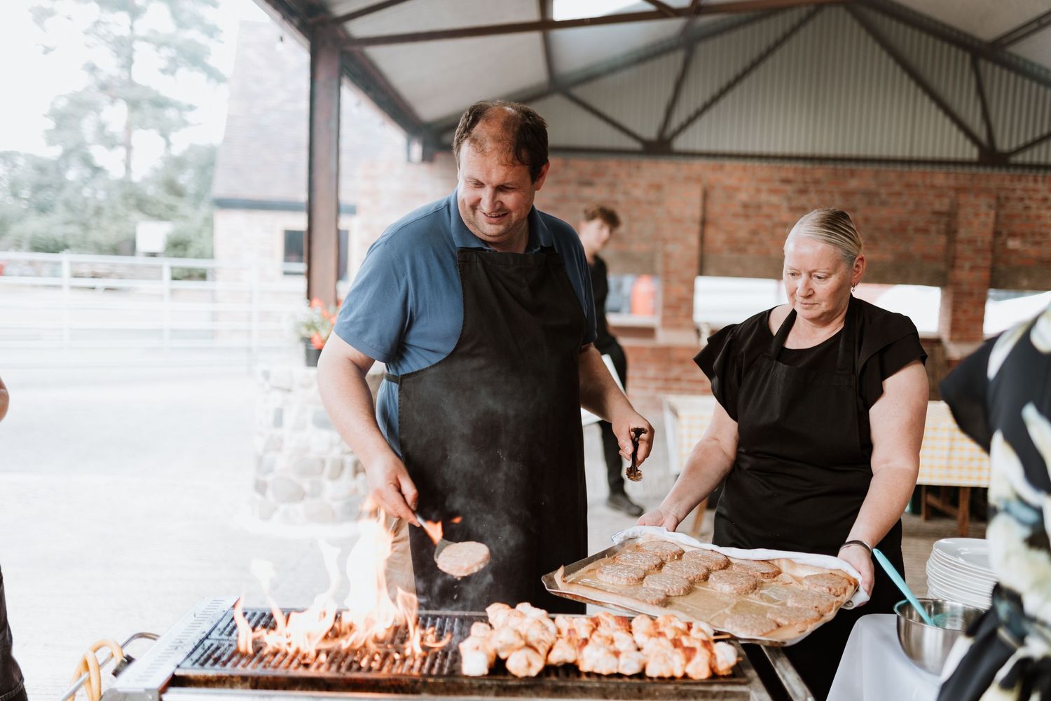 Ed of Oak Apple, grilling skewers and food on a large BBQ grill outdoors at a catering event.