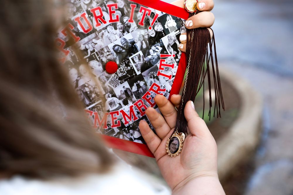 Close-up of a decorated graduation cap with photos and a tassel, held by a graduate during commencement ceremony.