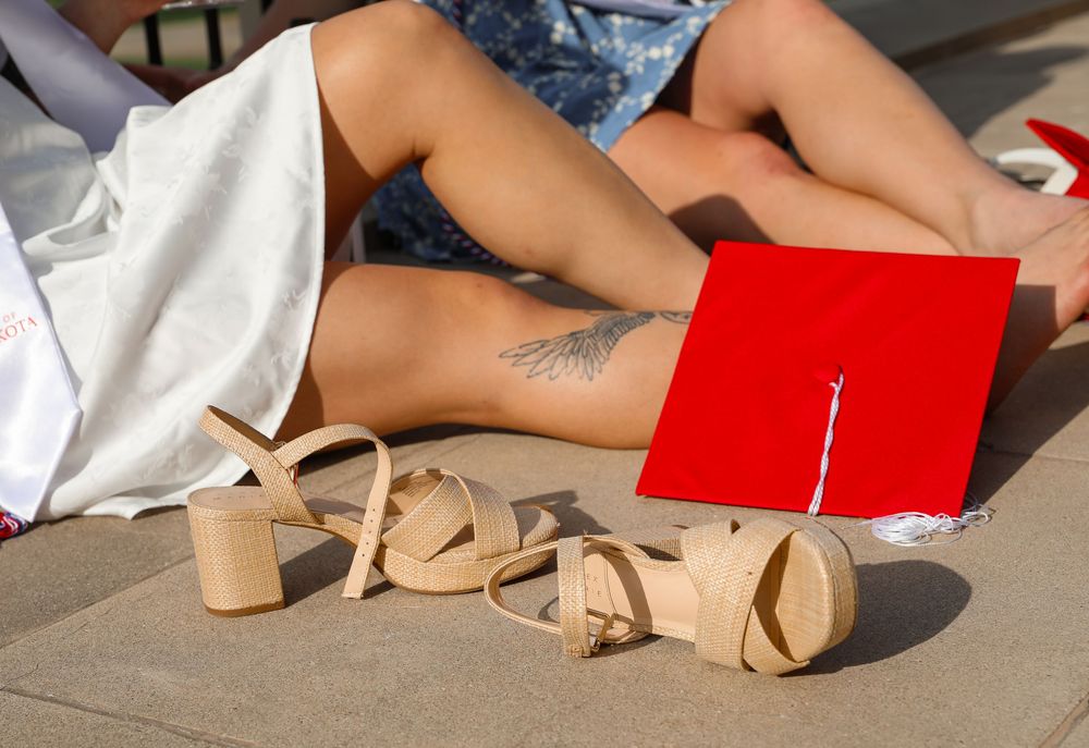 Close-up of graduation cap, nude heels, and ankle tattoo on steps at commencement ceremony.