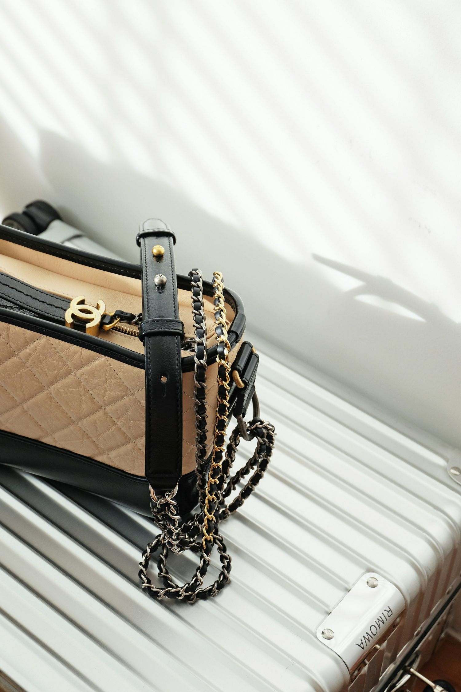 Chanel quilted beige handbag with gold chain strap resting on a white Rimowa luggage suitcase.