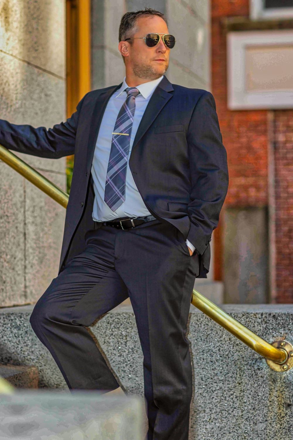 Business portrait series featuring sunglasses and navy suit against brick building.