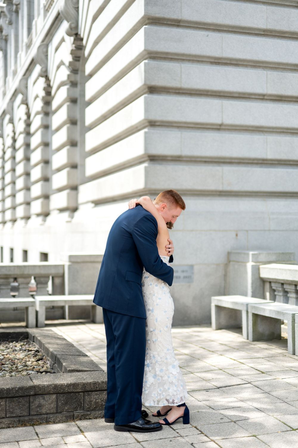 Bride and groom share a tender embrace outside a grand stone building on their wedding day.