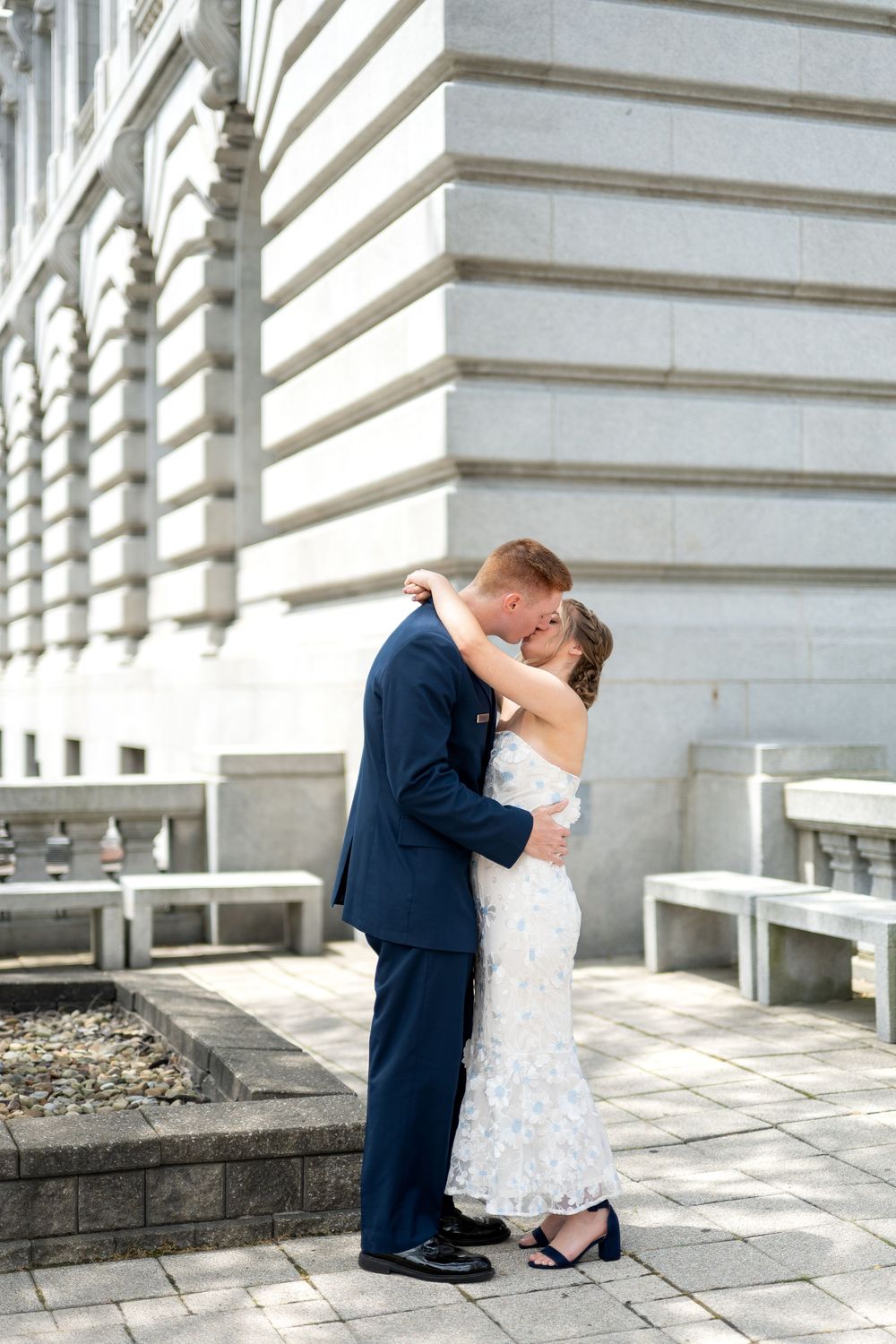 Bride and groom sharing a romantic kiss outside a grand stone building on their wedding day.