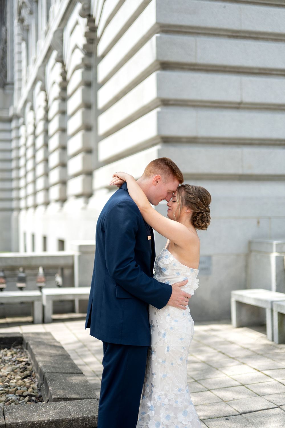 Newlyweds embracing tenderly in front of a classic stone building, bride in lace gown.