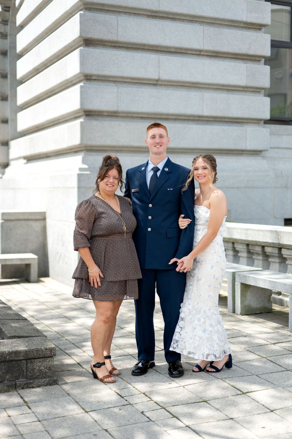 A man in military dress uniform stands smiling between two women outside a large stone government building.