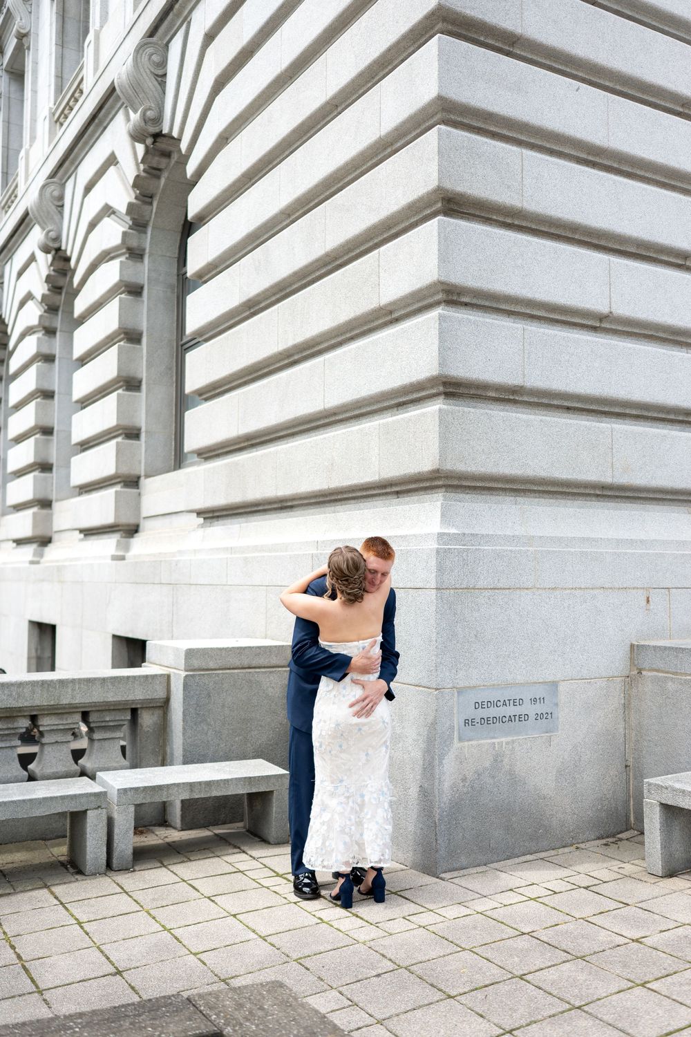 Bride and groom embrace near a classic stone building corner on their wedding day.