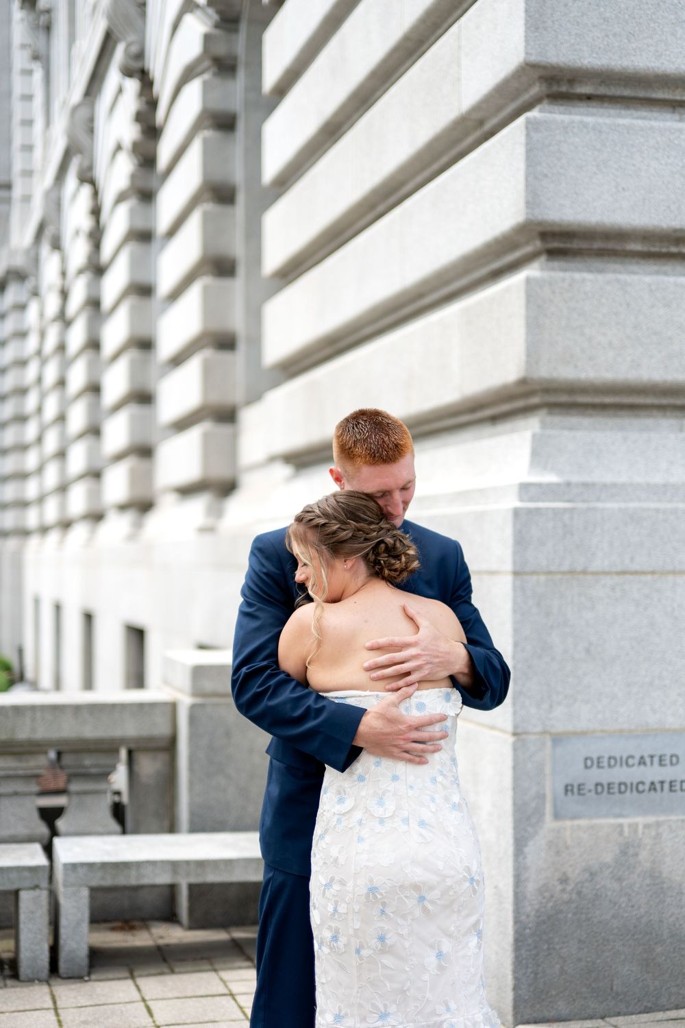Bride and groom share a tender embrace outside a grand stone building on their wedding day.