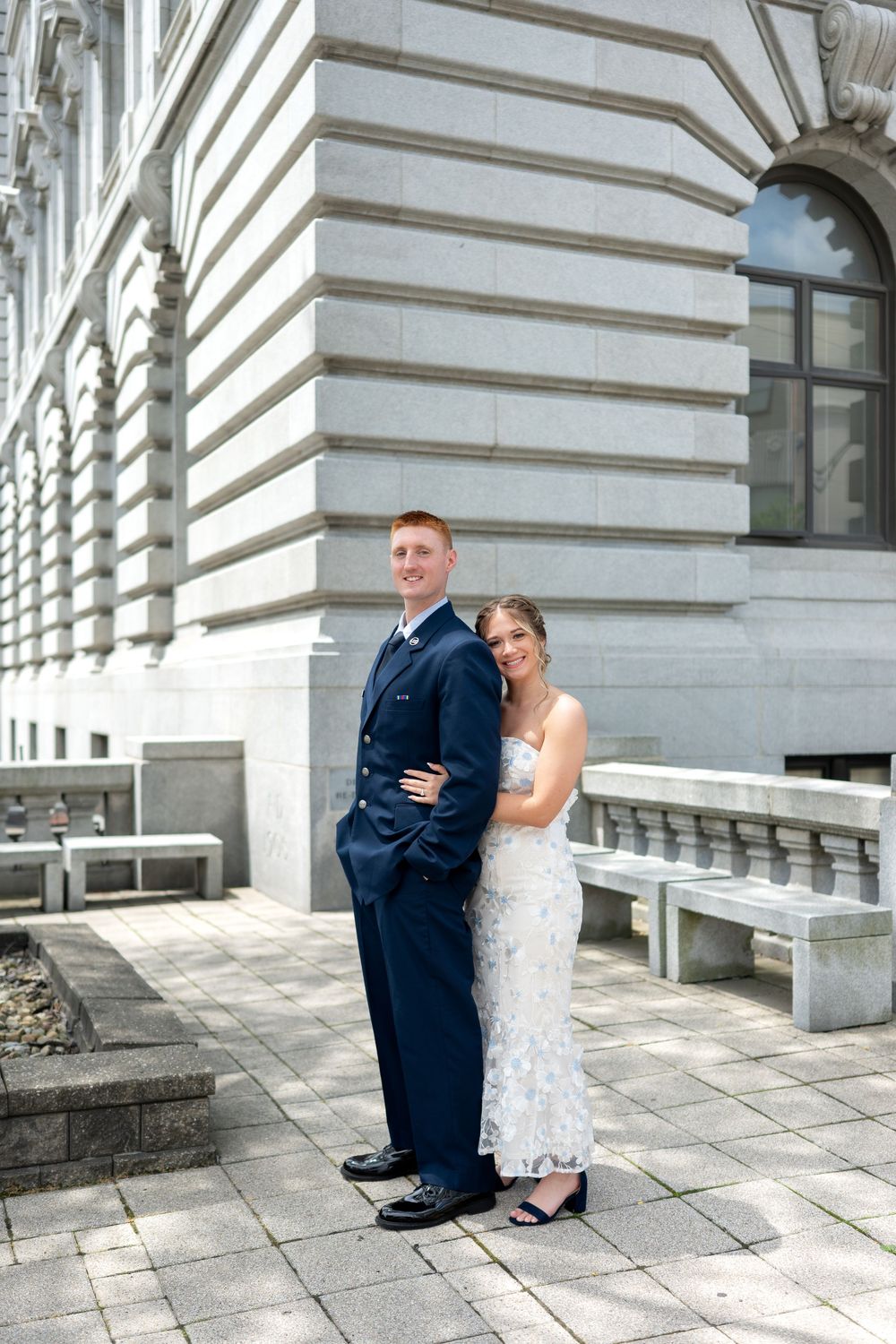 Bride and groom pose together outside a grand stone building on their wedding day.
