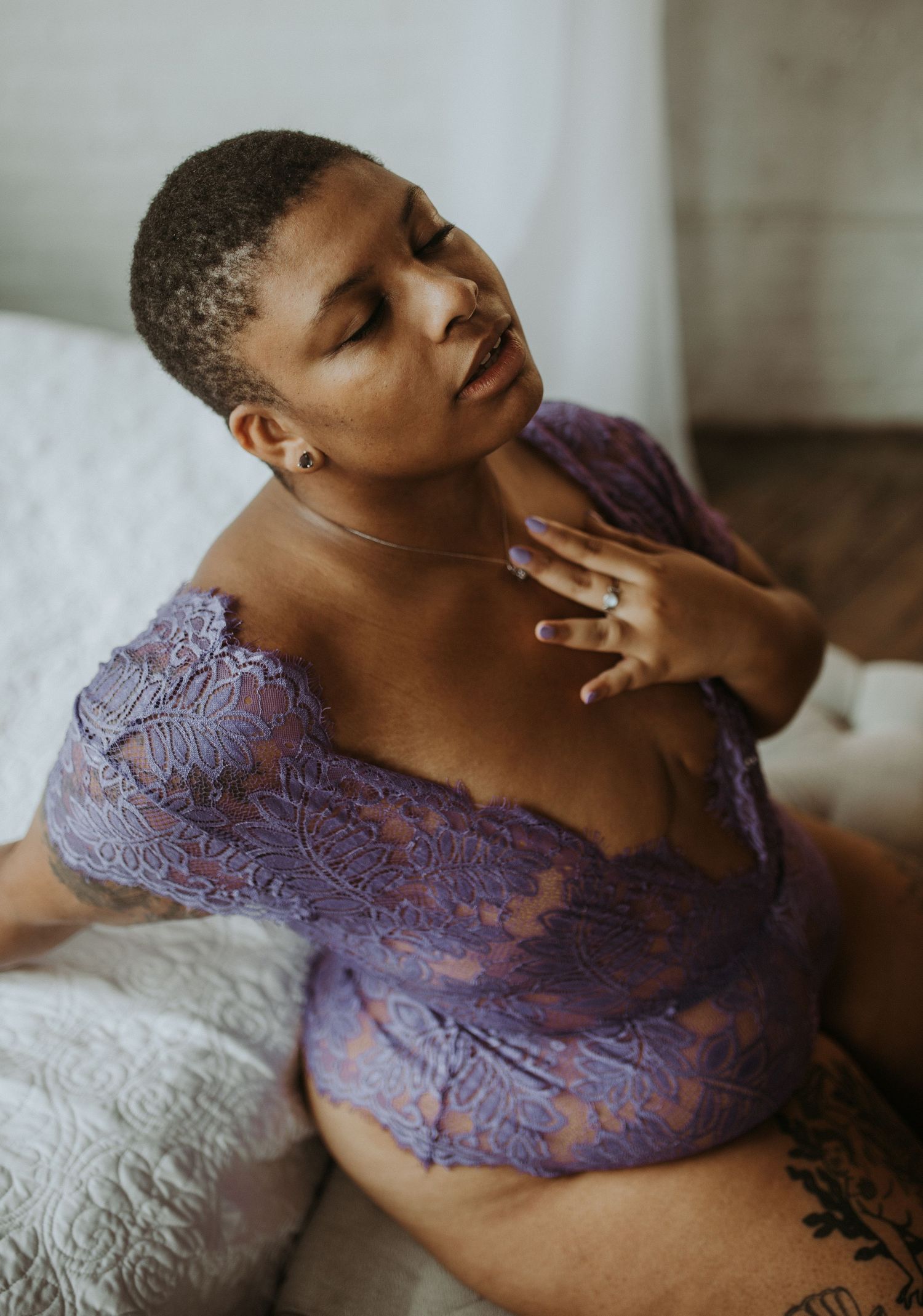 A woman in purple lace lingerie poses gracefully on a bed, showcasing elegant boudoir photography.