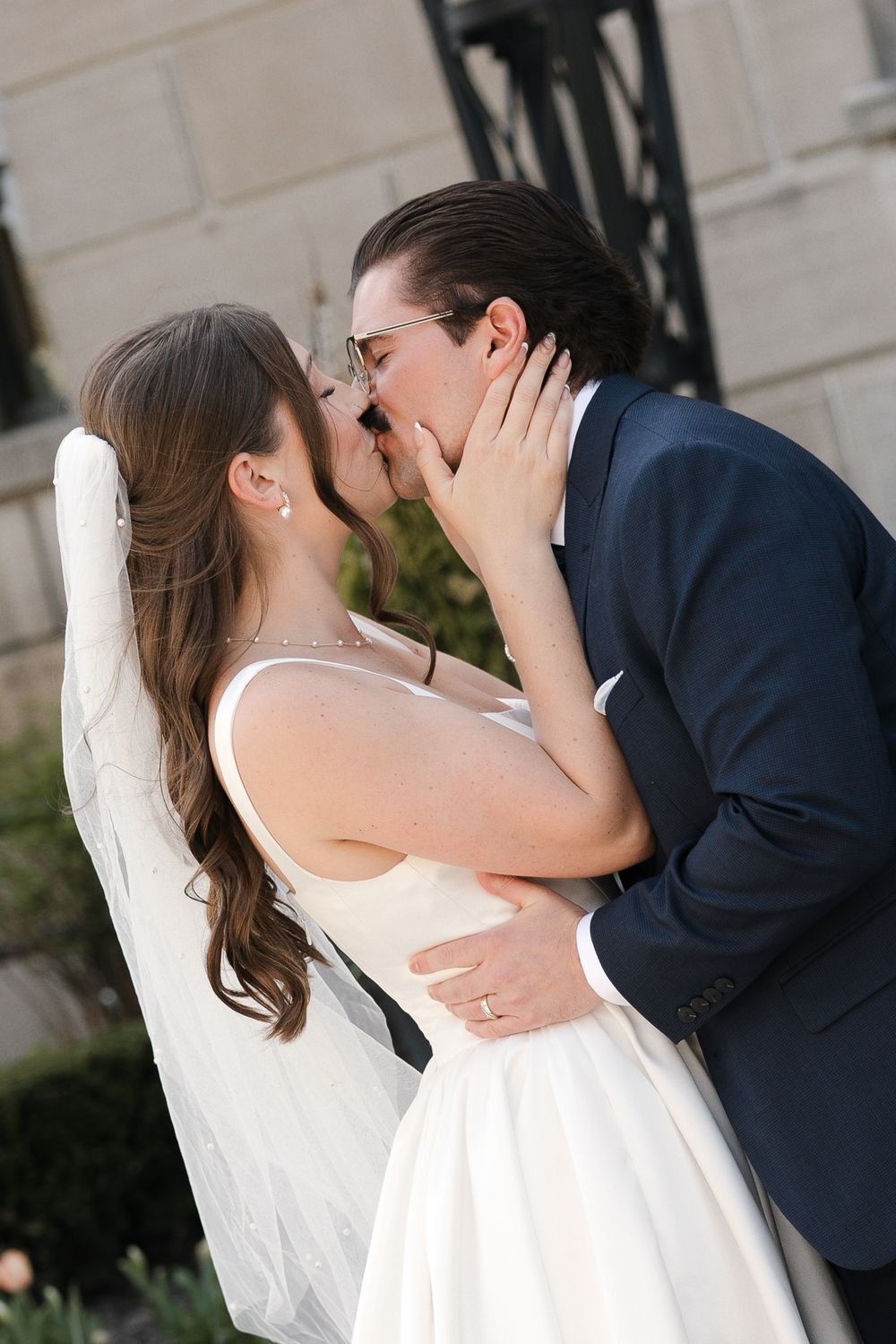 Bride and groom share a passionate kiss outdoors with the bride's veil flowing on their wedding day.