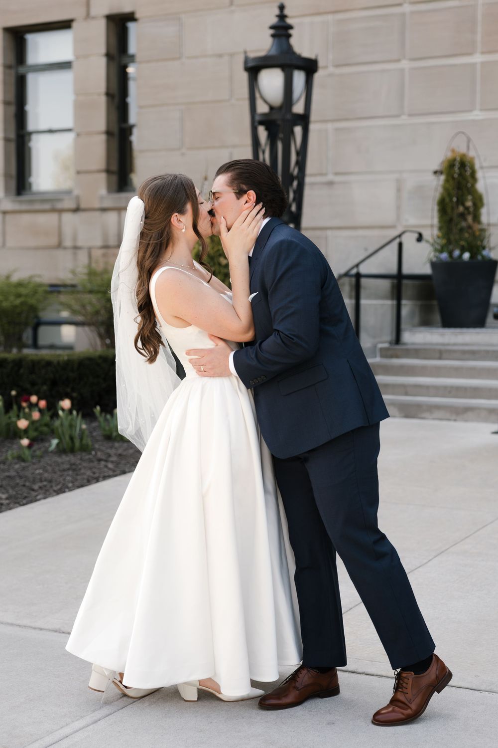 Bride and groom sharing a romantic first kiss outside a stone building on their wedding day.