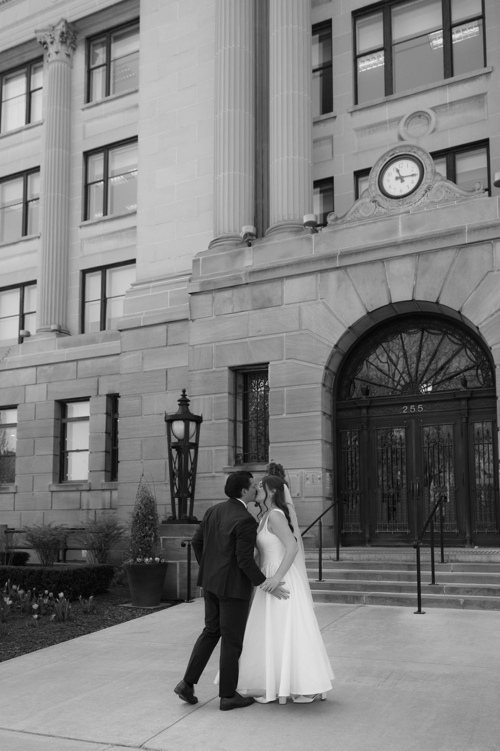 Black and white photo of bride and groom kissing outside a grand stone courthouse building.