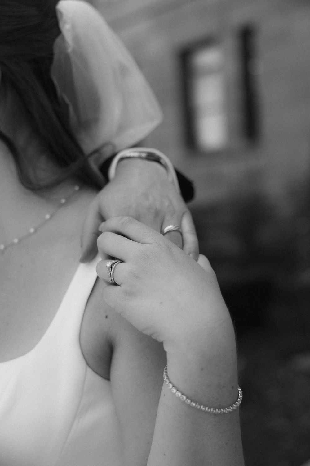 Black and white close-up of bride and groom hands showing wedding rings.