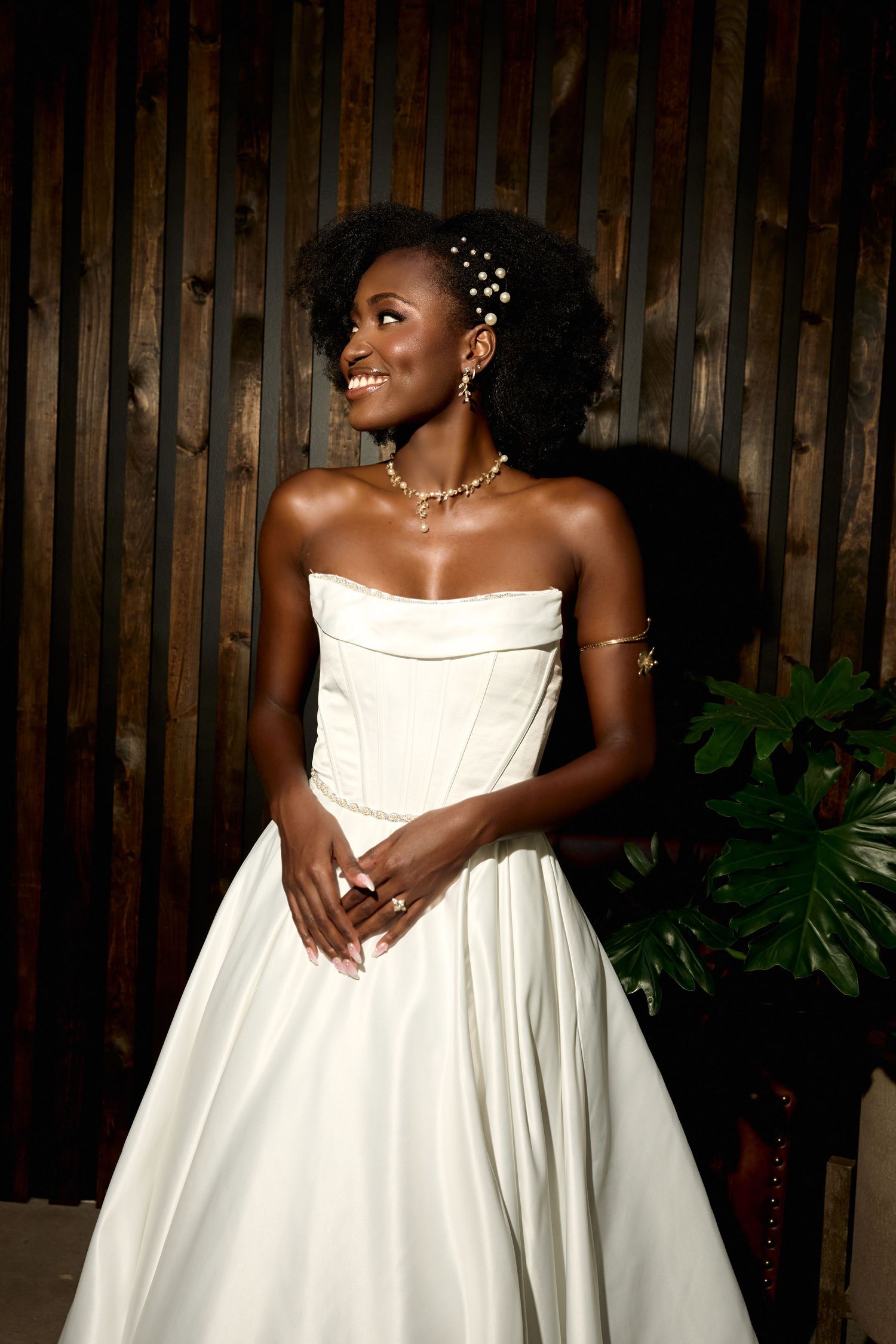 A joyful bride in a strapless white gown holds a drink at an outdoor wedding reception with string lights.