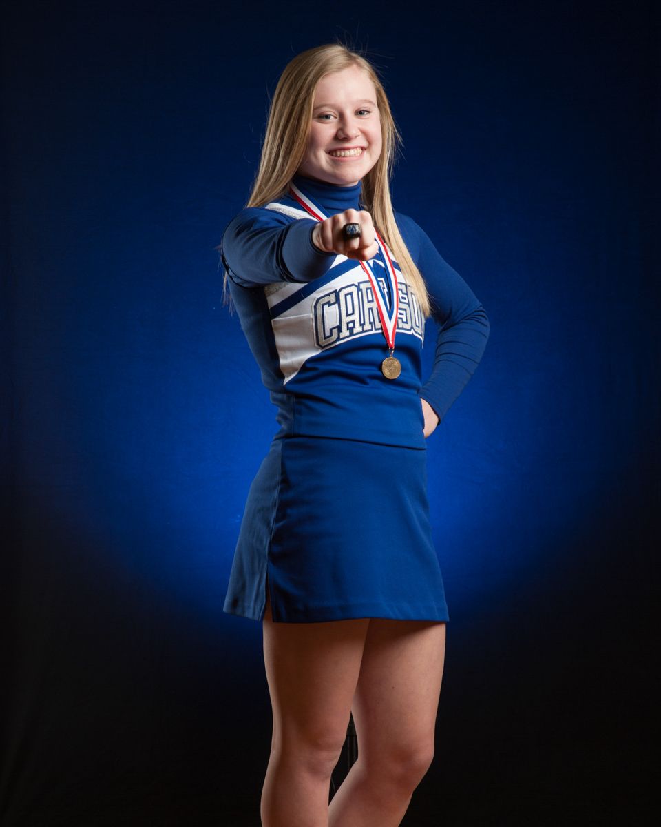 Young cheerleader in blue Carlson uniform pointing a medal toward the camera.