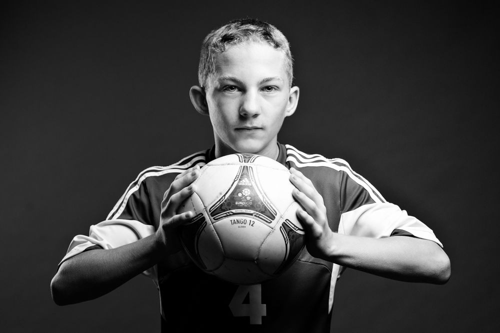 Young male soccer player holds ball in black and white sports portrait photo.