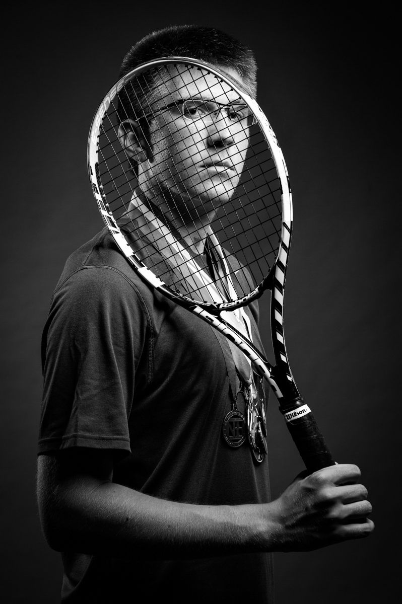 Black and white portrait of a tennis player holding a racket in front of his face.