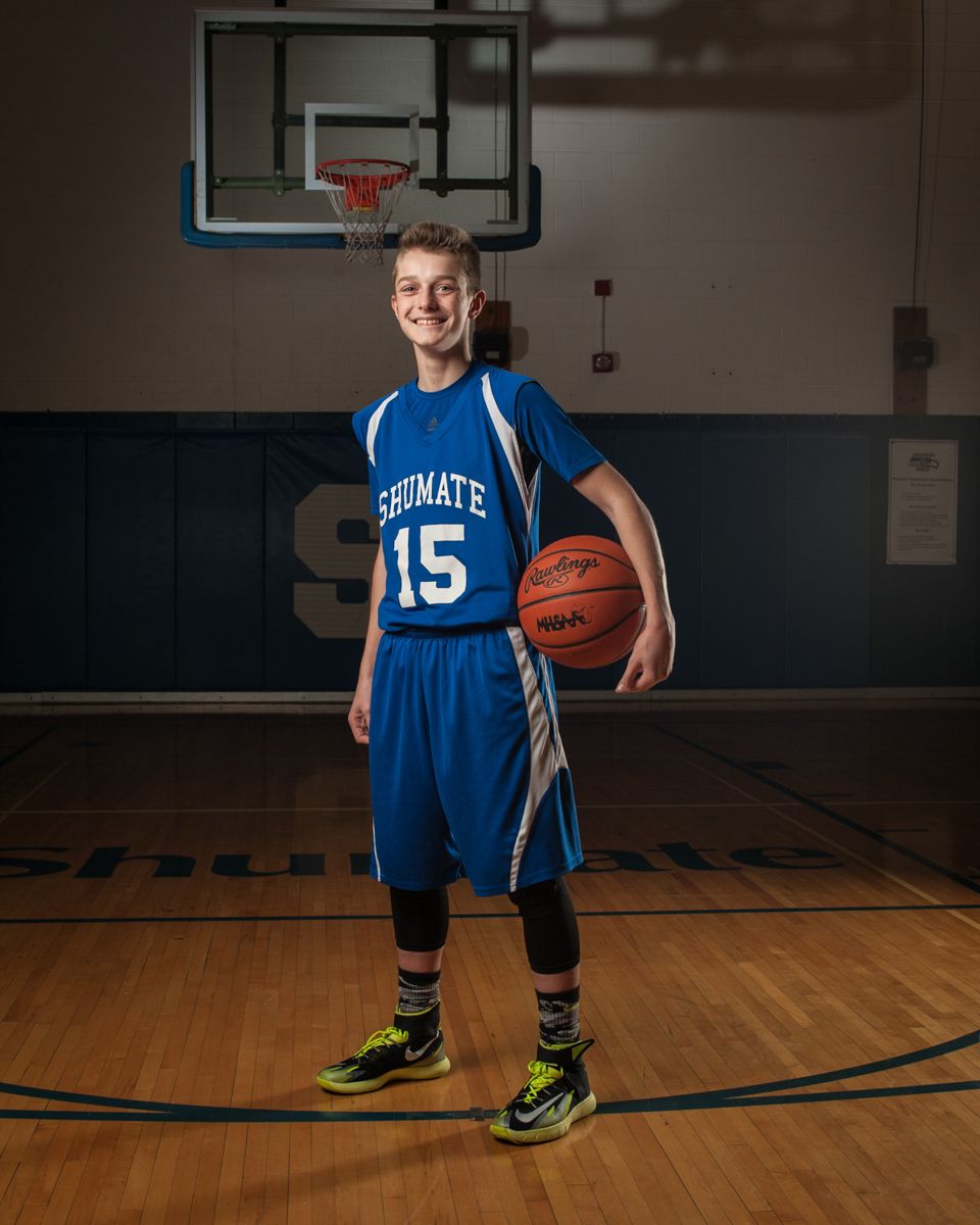 Smiling basketball player in blue number 15 jersey holding a ball in a gymnasium.