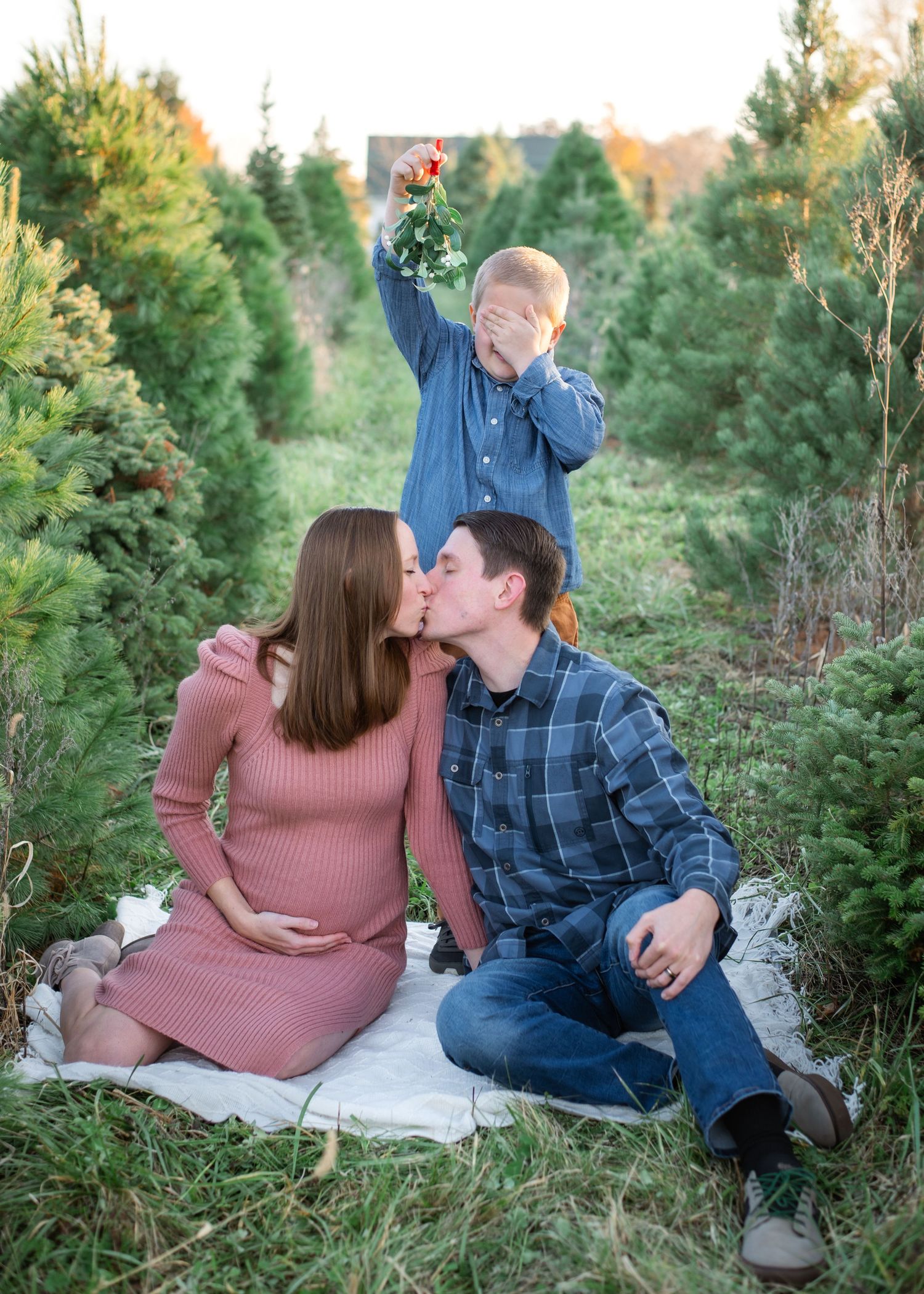 Pregnant woman in purple sweater with husband's hands on baby bump, both wearing wedding rings.