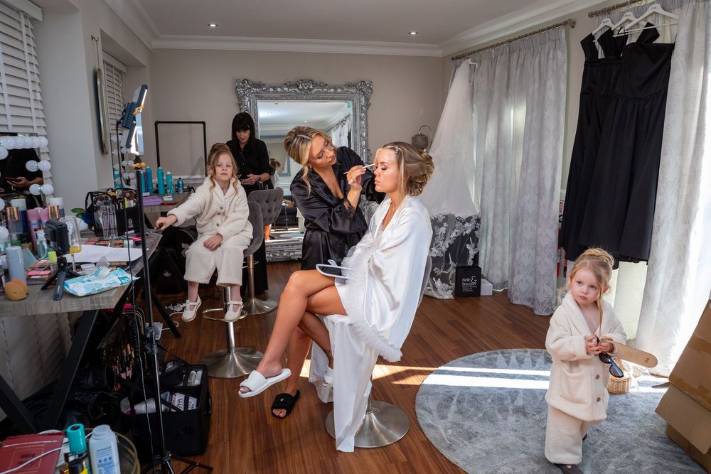 Bridesmaids in robes getting hair and makeup done in a bright dressing room before a wedding.