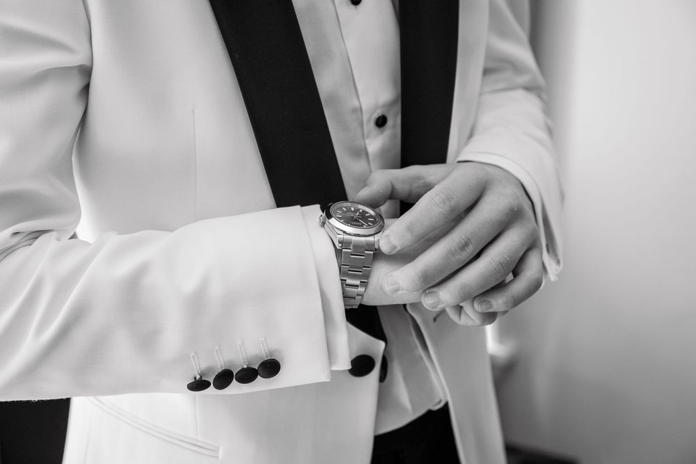 Black and white photo of a groom in a white tuxedo adjusting his luxury watch before the wedding ceremony.