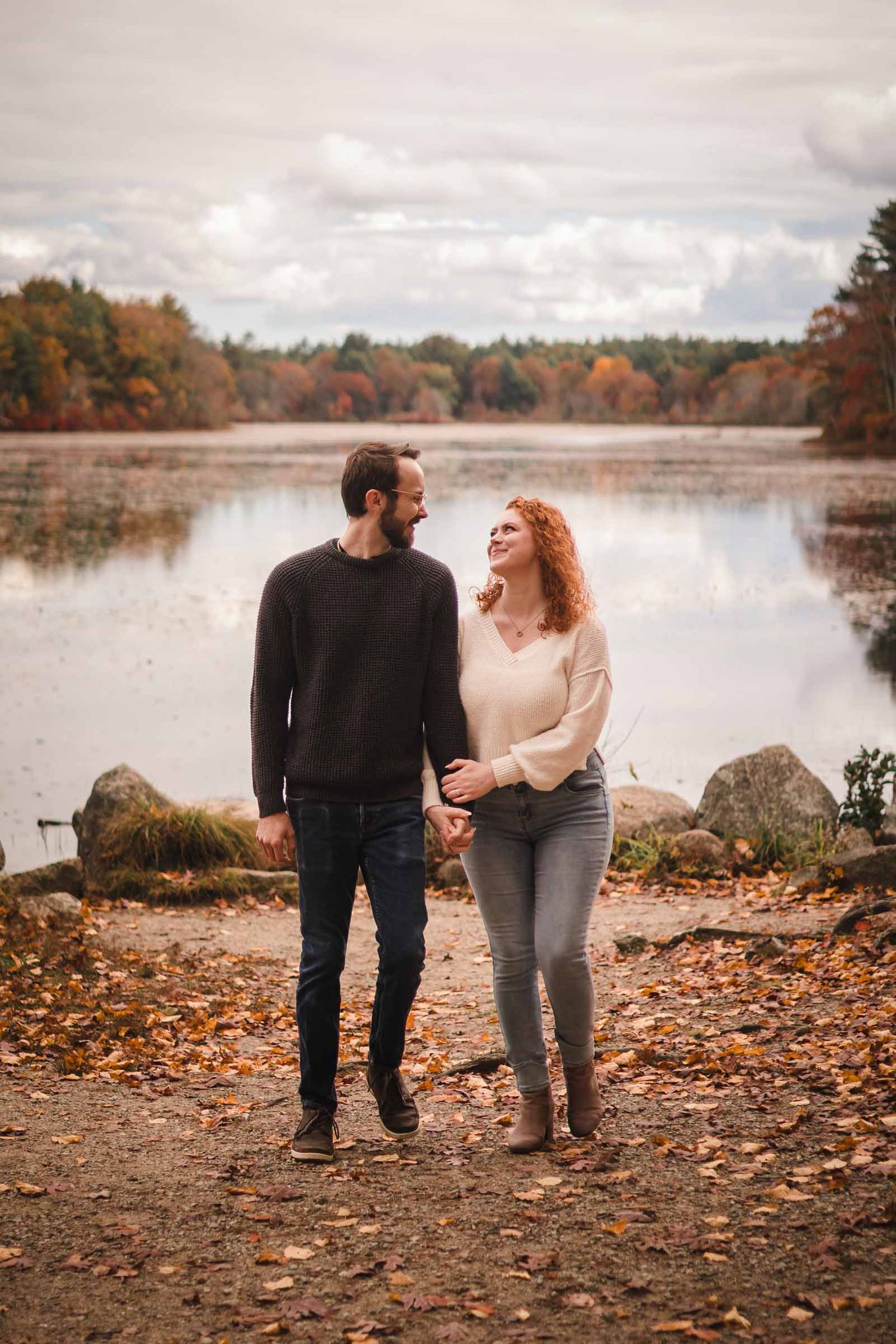 Engaged couple walking hand in hand along the shore of Lake Leach at Borderland State Park, looking at each other and smiling.