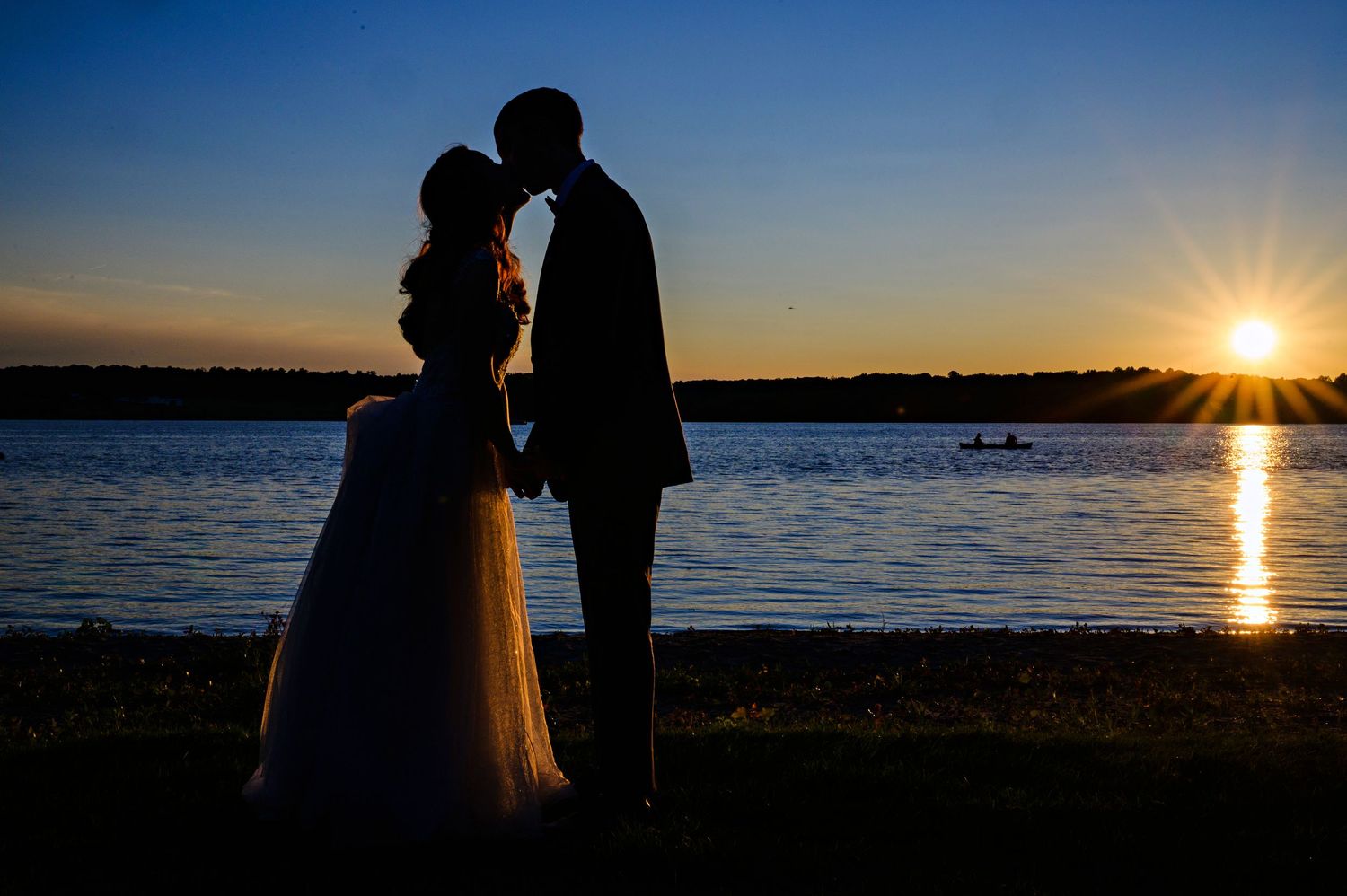 Bride and Groom kiss at sunset over Chippewa Lake during their wedding ceremony and reception at The Oaks Lakeside on a summer day in Ohio